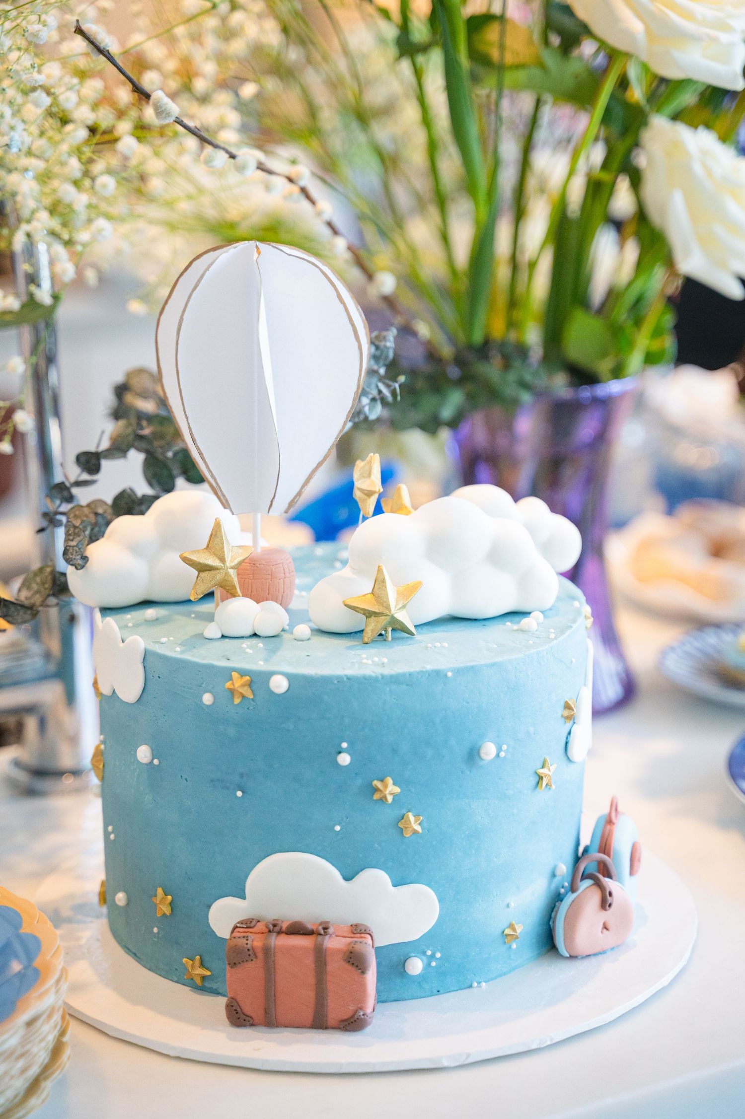 Blue travel themed celebration cake with floral details displayed at baby shower.