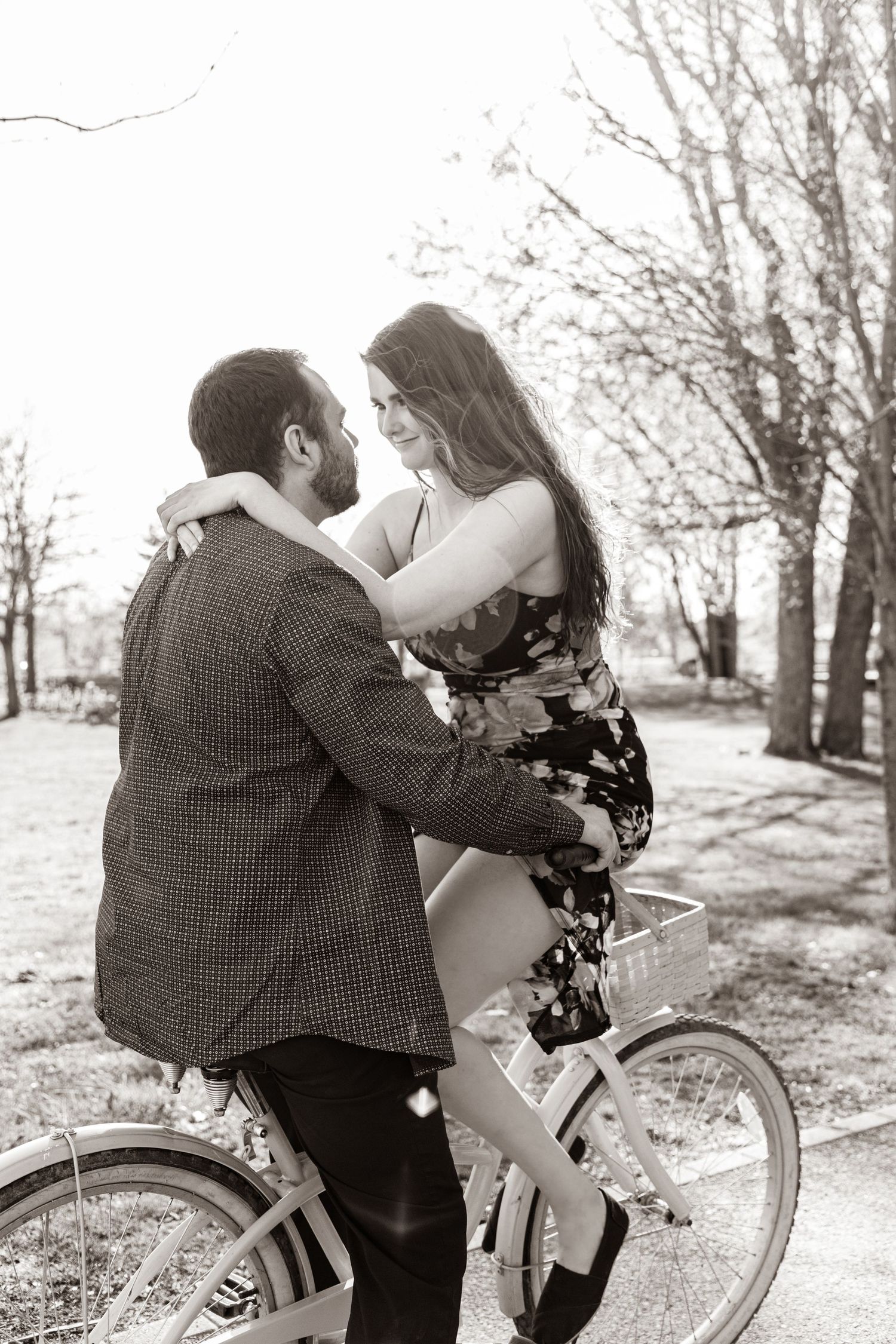 A romantic black and white photo of a couple sharing an intimate moment on a bicycle in a park setting.