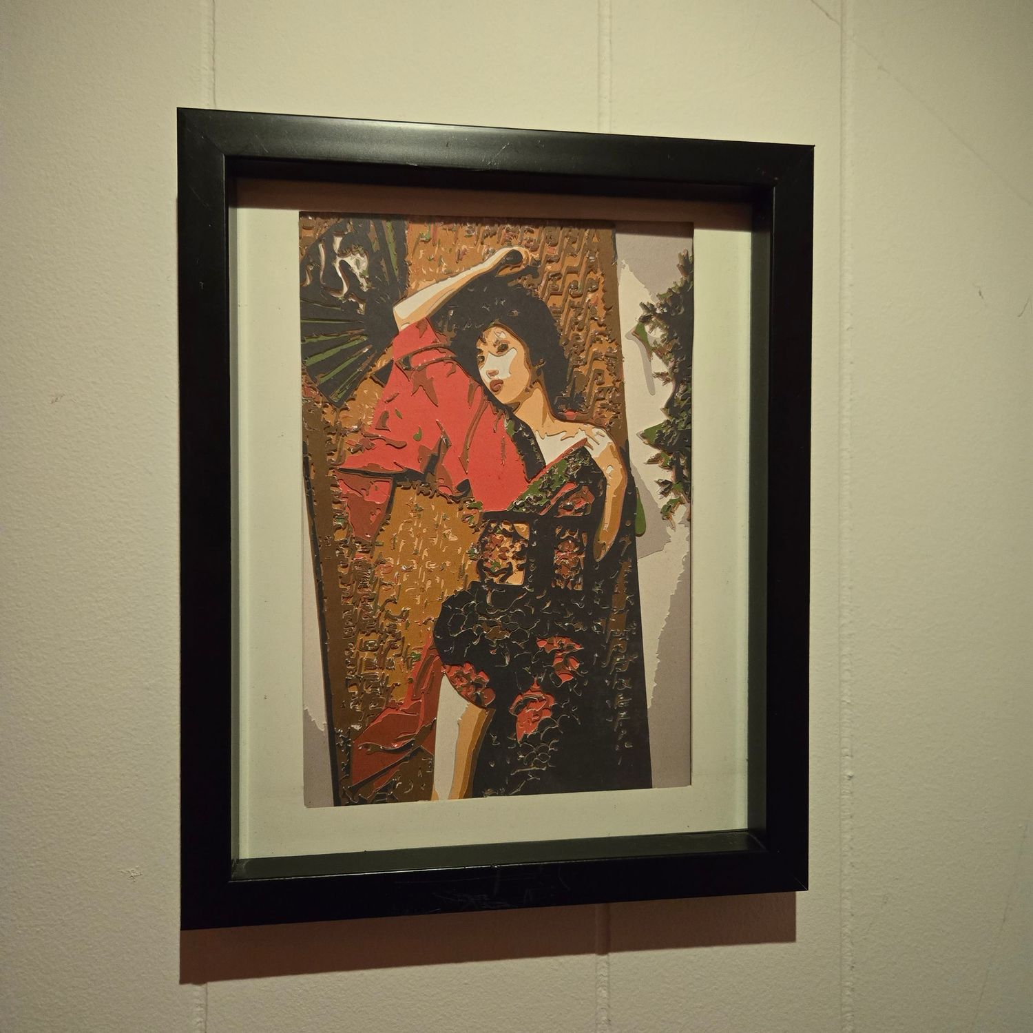 Framed artwork of a flamenco dancer in red and black dress with fan, displayed on white gallery wall.