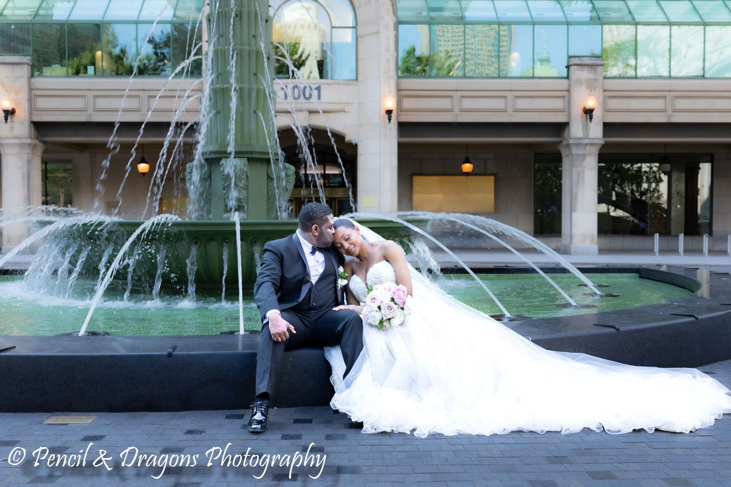 Wedding party poses along a modern glass building exterior with fountains.