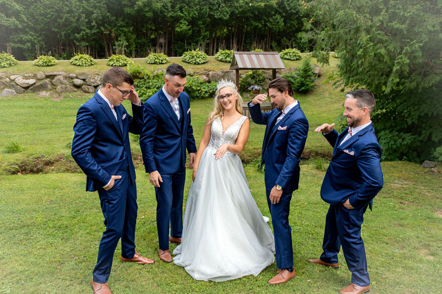 Wedding party in navy suits posing playfully on green lawn.