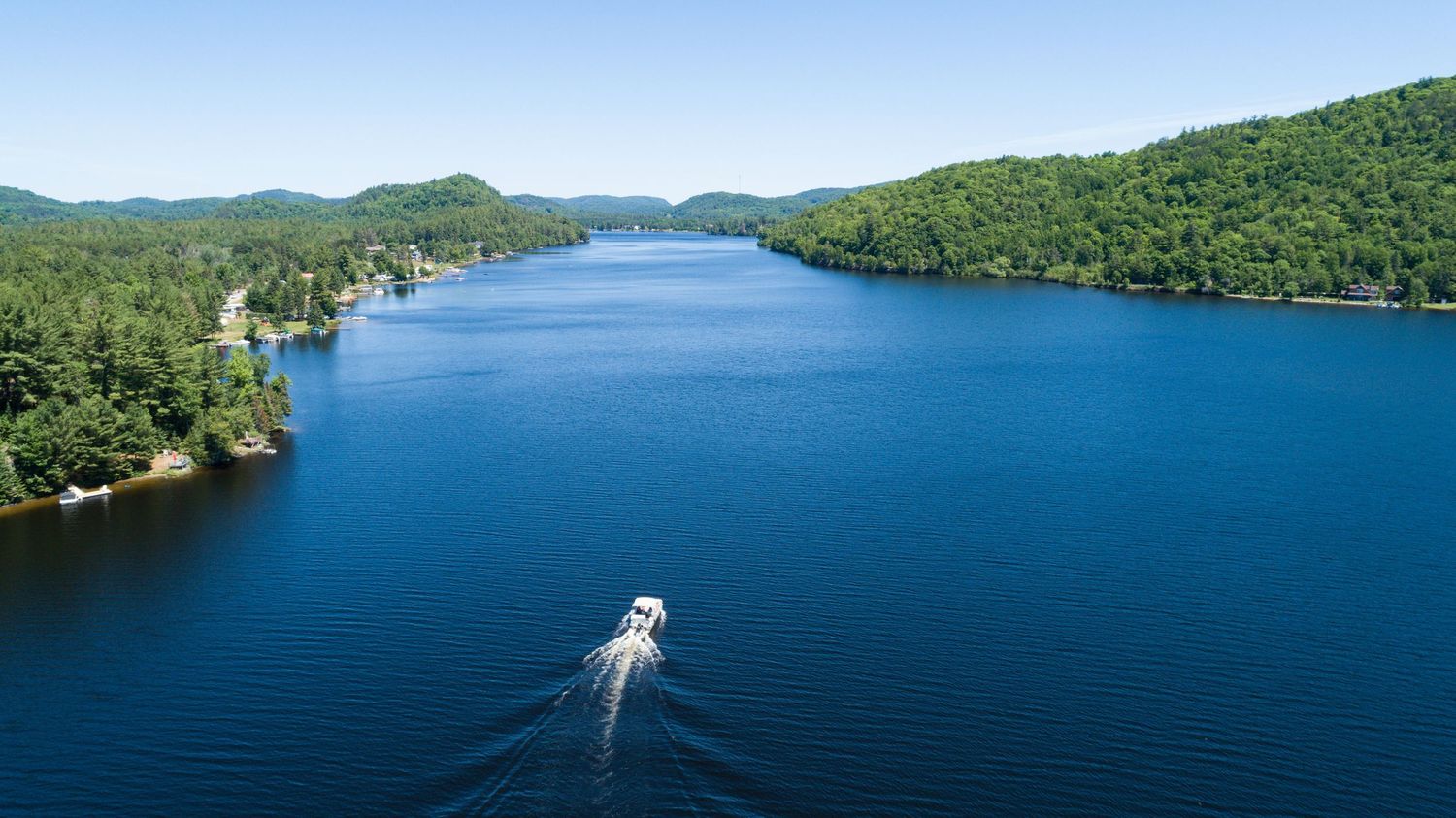 Panoramic view of a serene lake surrounded by lush green mountains and forests.