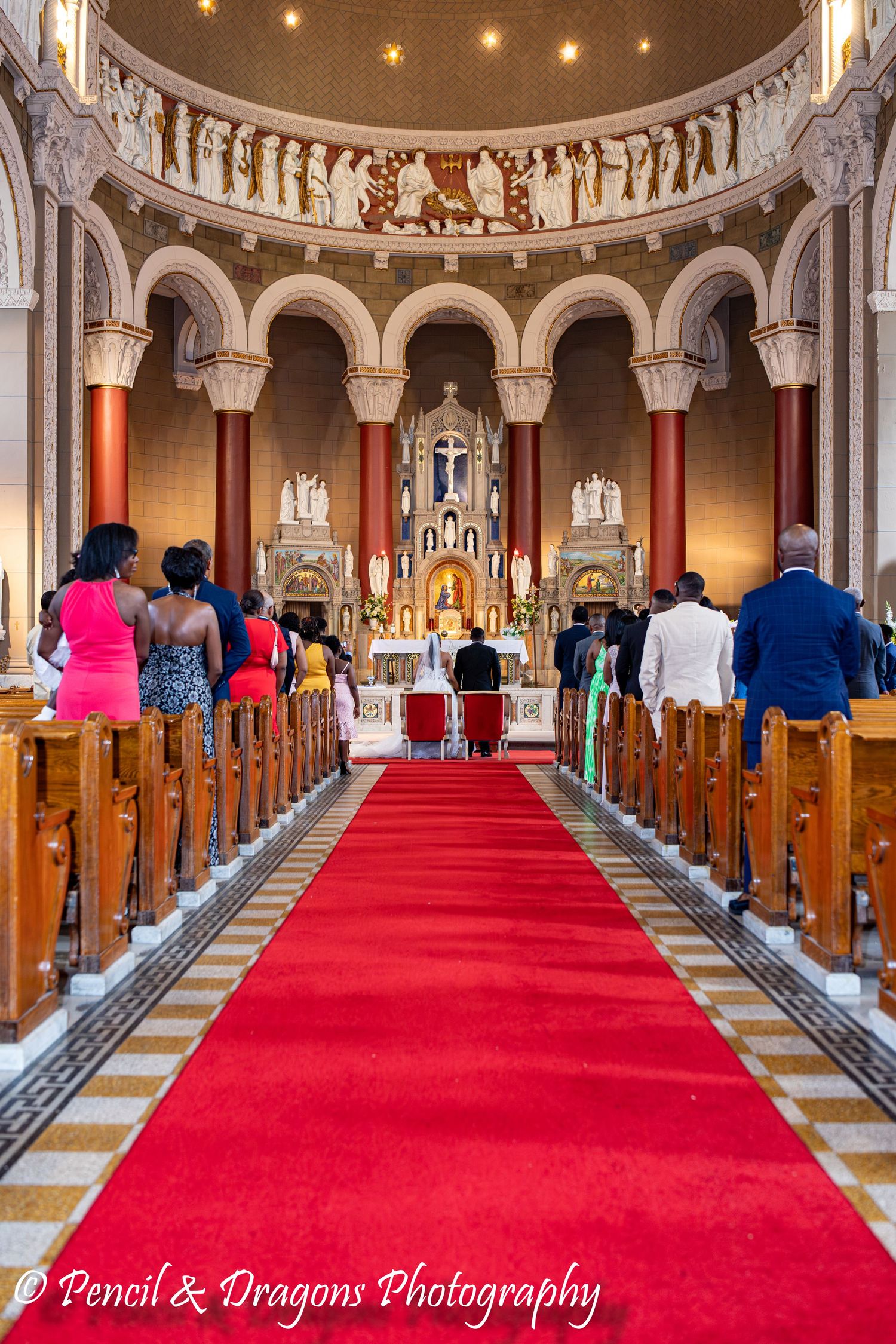 Ornate church interior with red carpet aisle and decorative columns illuminated by string lights.