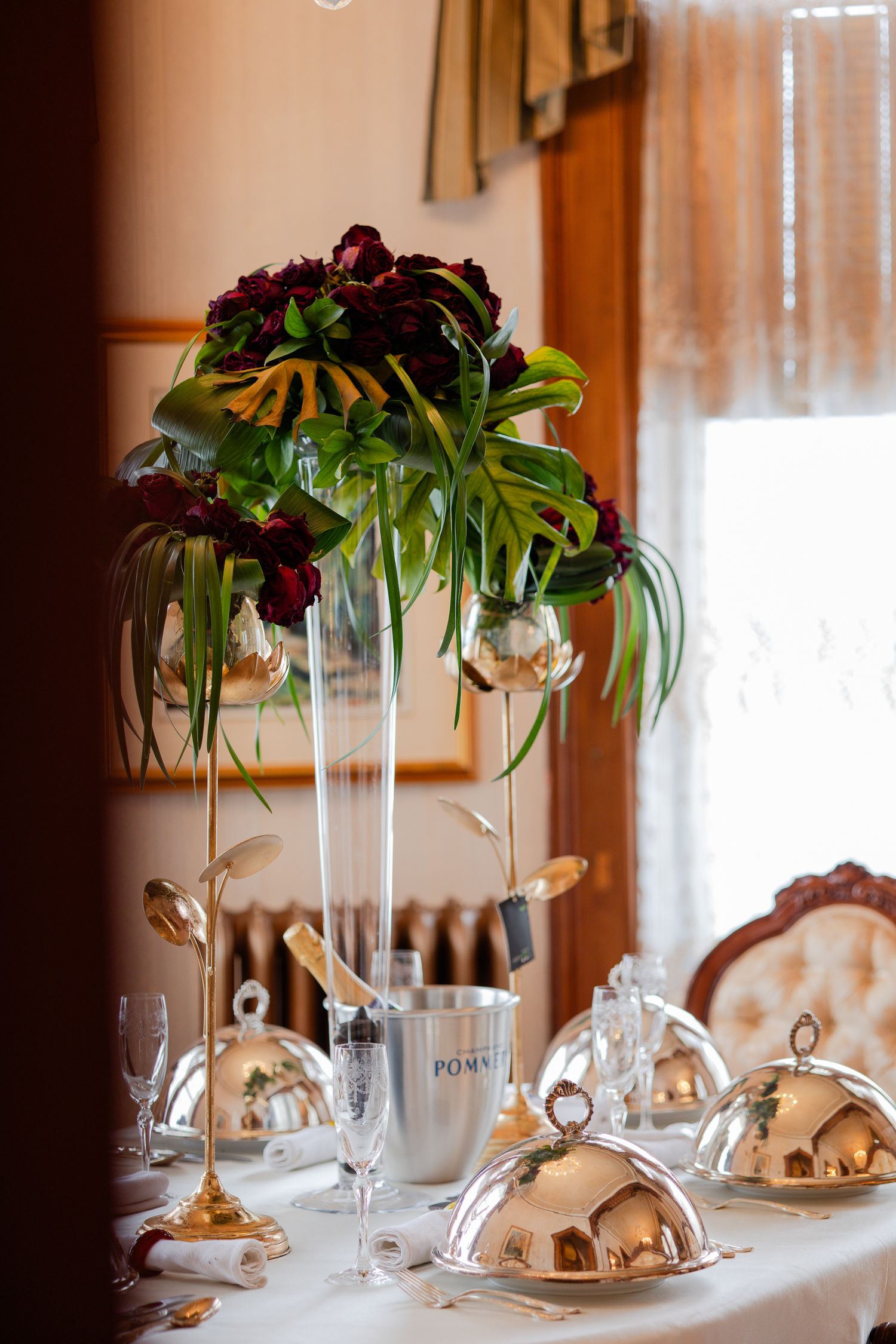 Elegant table settings with silver cloches and tall floral centerpieces in glass vases at a formal dining event.