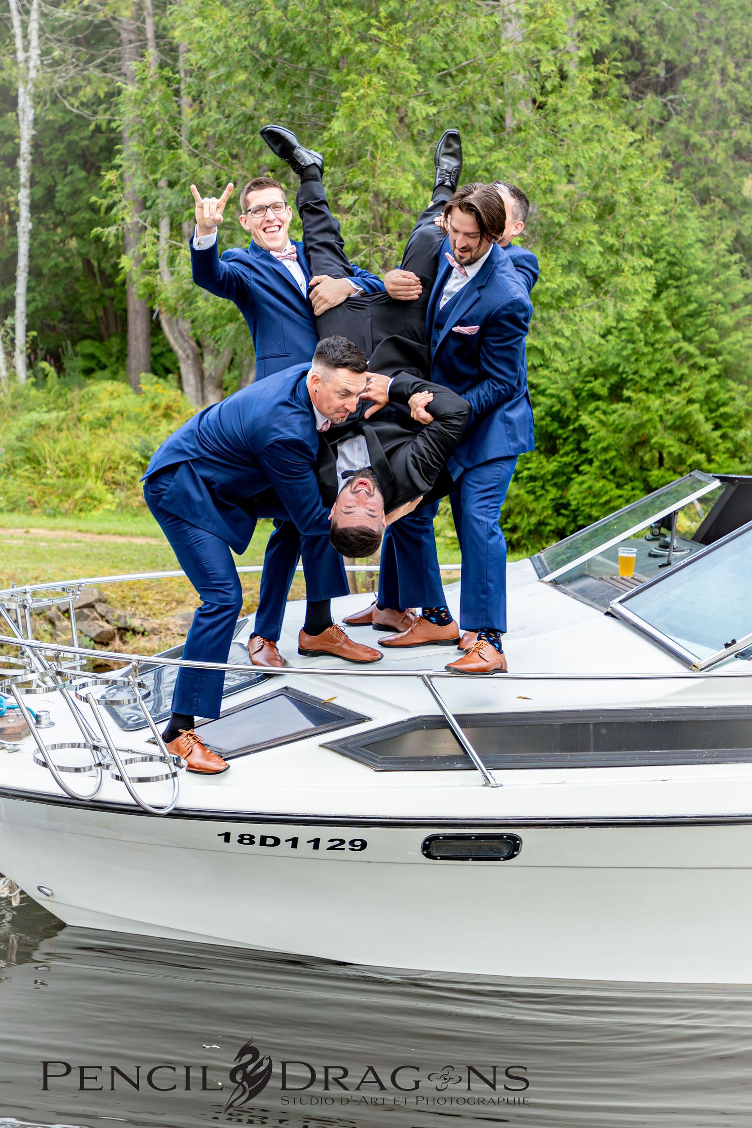 Groomsmen in navy suits pose playfully on a white boat during wedding celebrations.