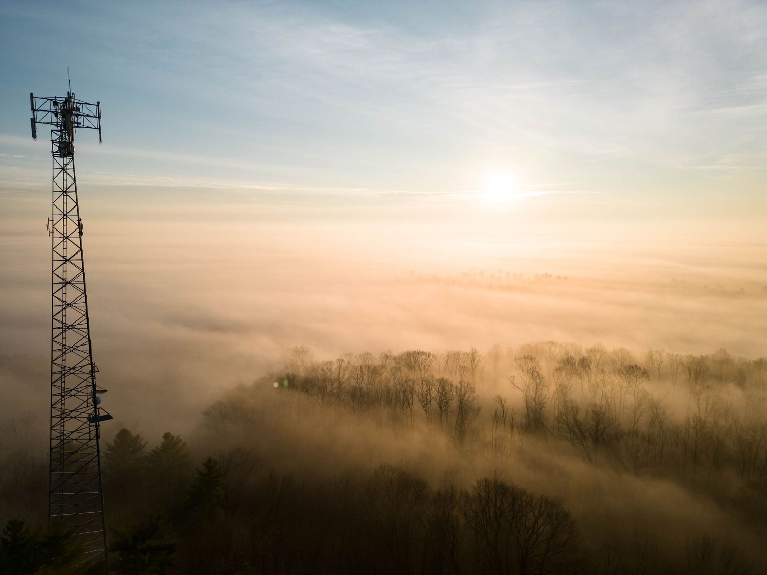 Misty sunrise landscape with electrical tower silhouetted against foggy valley.