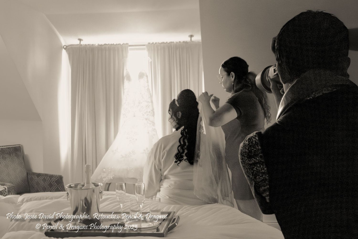 Black and white photograph of wedding preparation scene in a bright room with curtains.