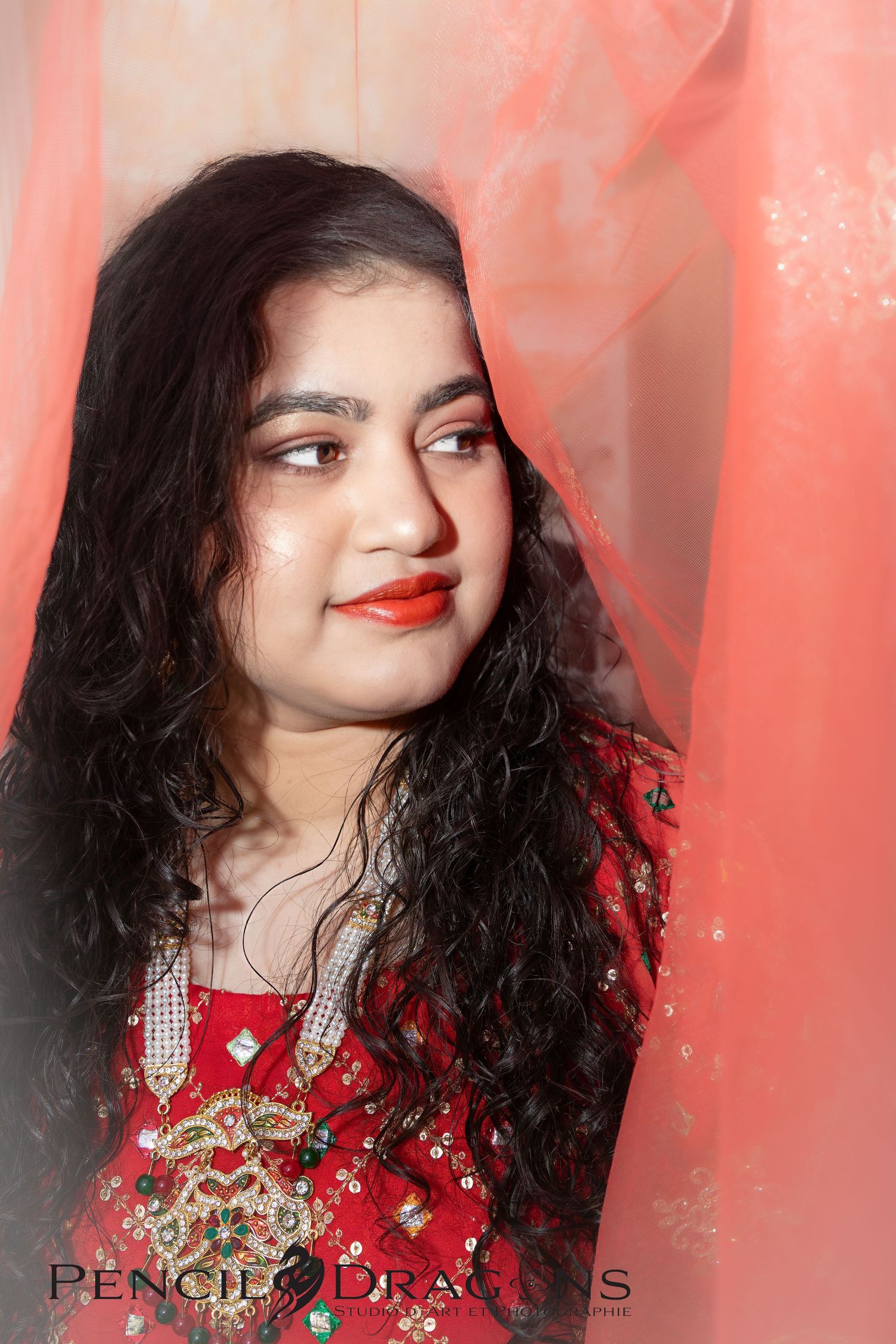 A portrait against coral backdrop featuring traditional South Asian formal attire and jewelry.