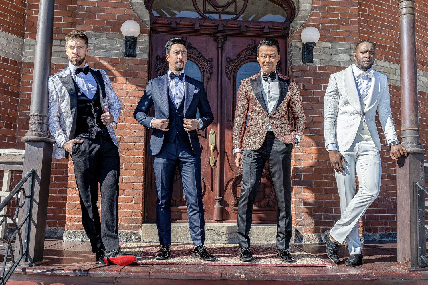 A group of groomsmen in formal suits pose together on brick steps for a wedding photo.