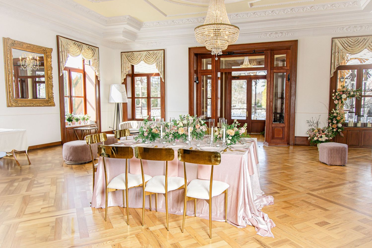Elegant ballroom interior with hardwood floors, ornate moldings, and floor-to-ceiling windows reflecting natural light.