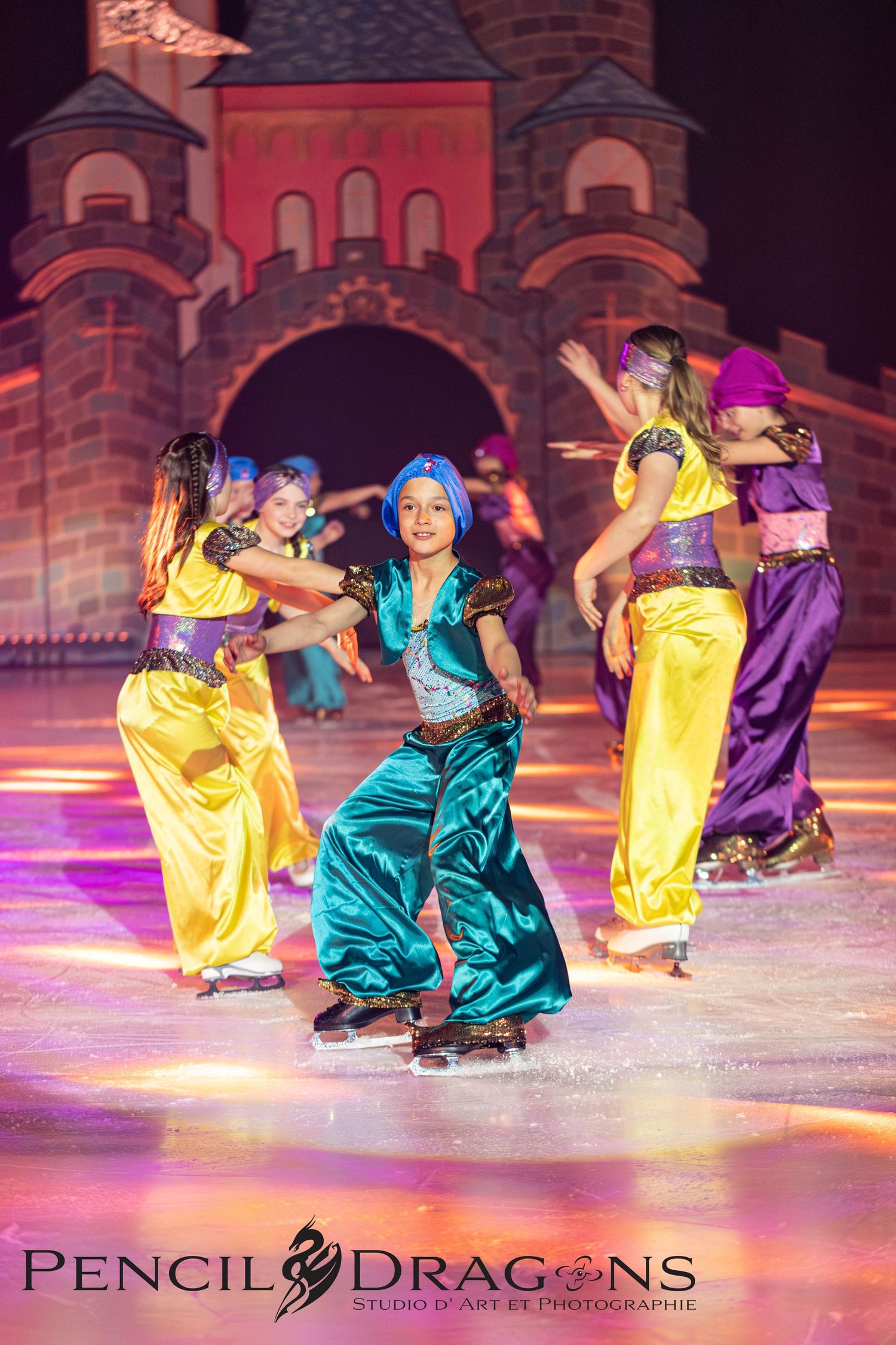 Young girls in colorful Arabian-style costumes perform an ice skating routine on stage at a Disney on Ice show.