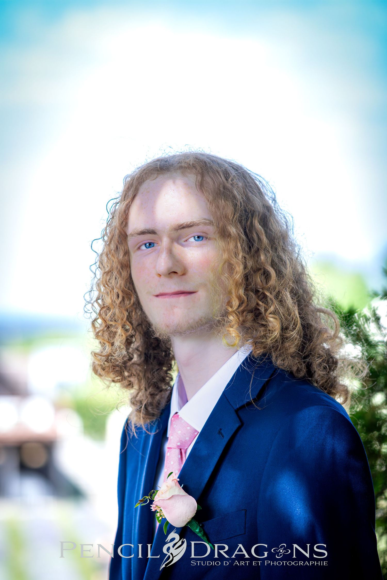 Professional headshots of person in navy suit with pink tie against light blue background.