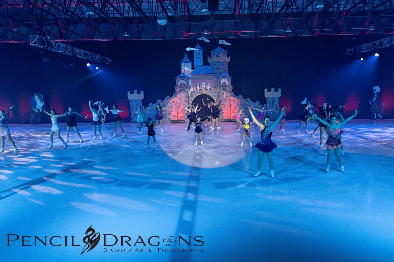 Ice skaters perform in front of a lit castle backdrop at an indoor arena show by Pencil Dragons.