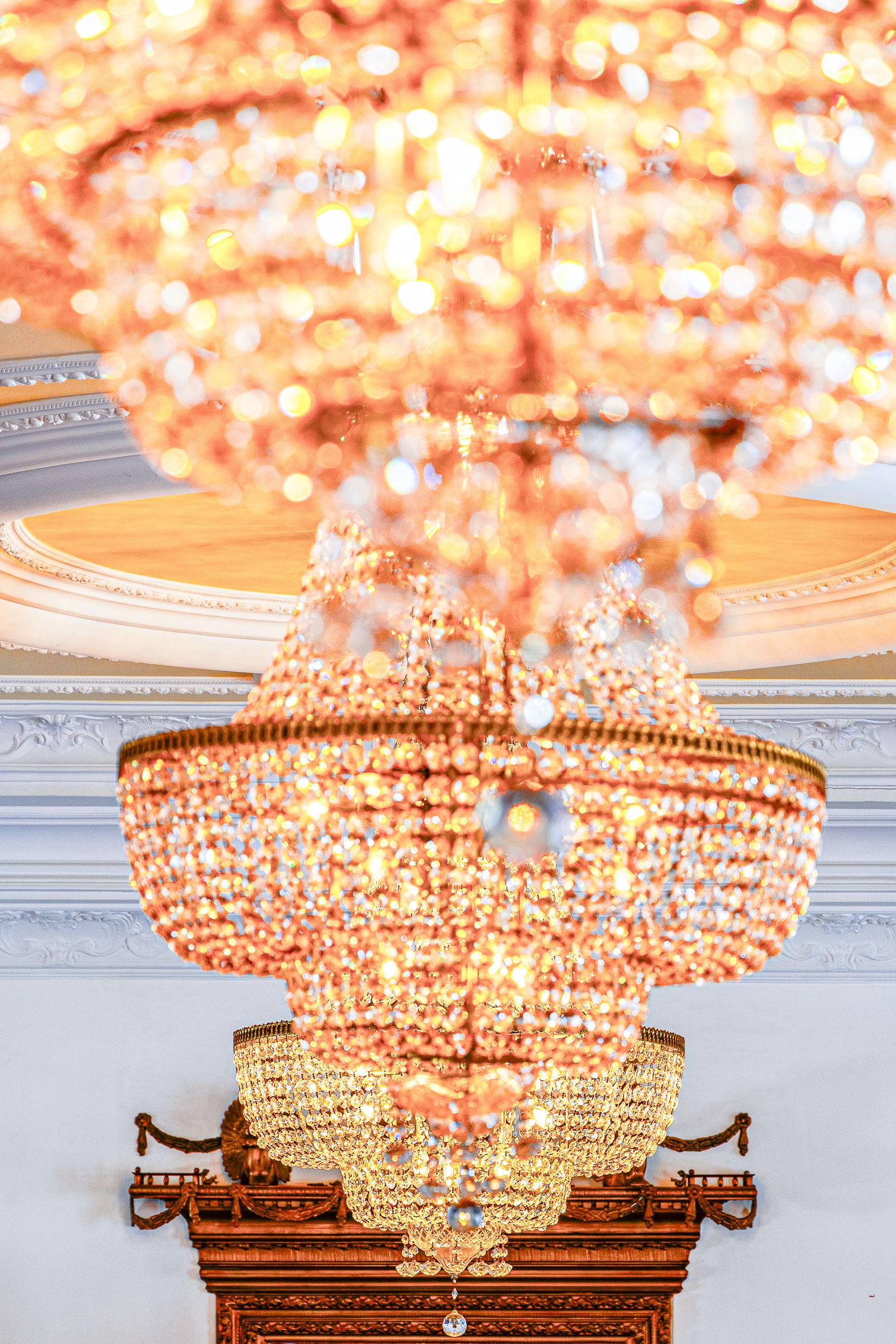 Ornate crystal chandeliers with warm glowing lights create an elegant ambiance in a luxurious interior setting.