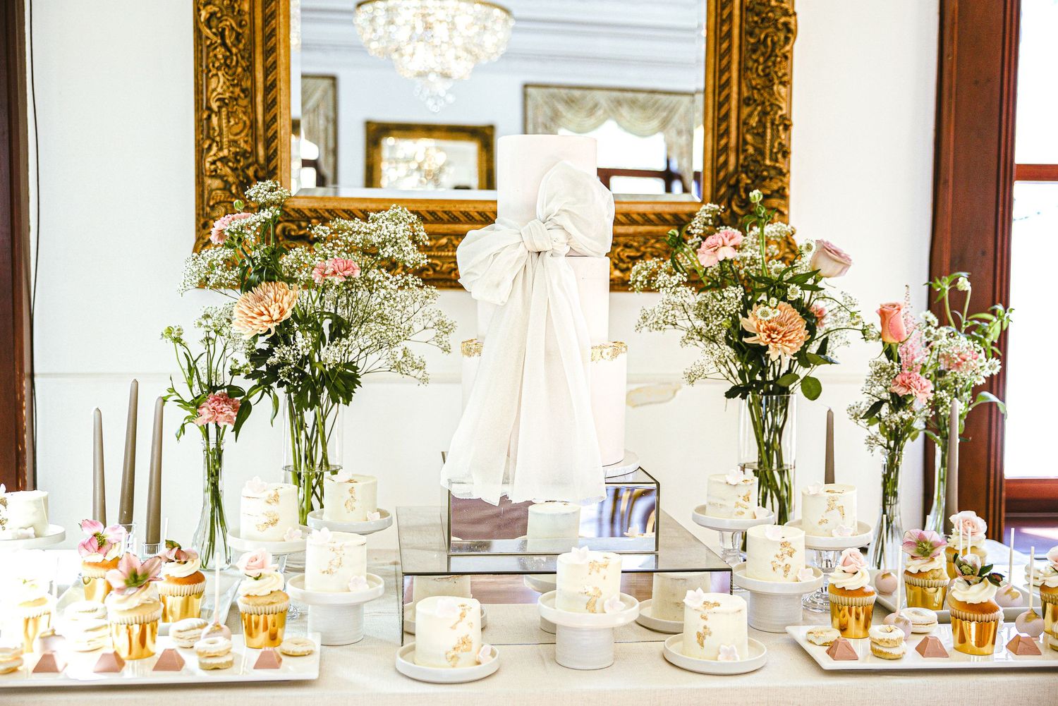 Elegant wedding reception table setting with crystal chandeliers, floral centerpieces, and gold accents in a luxurious ballroom.