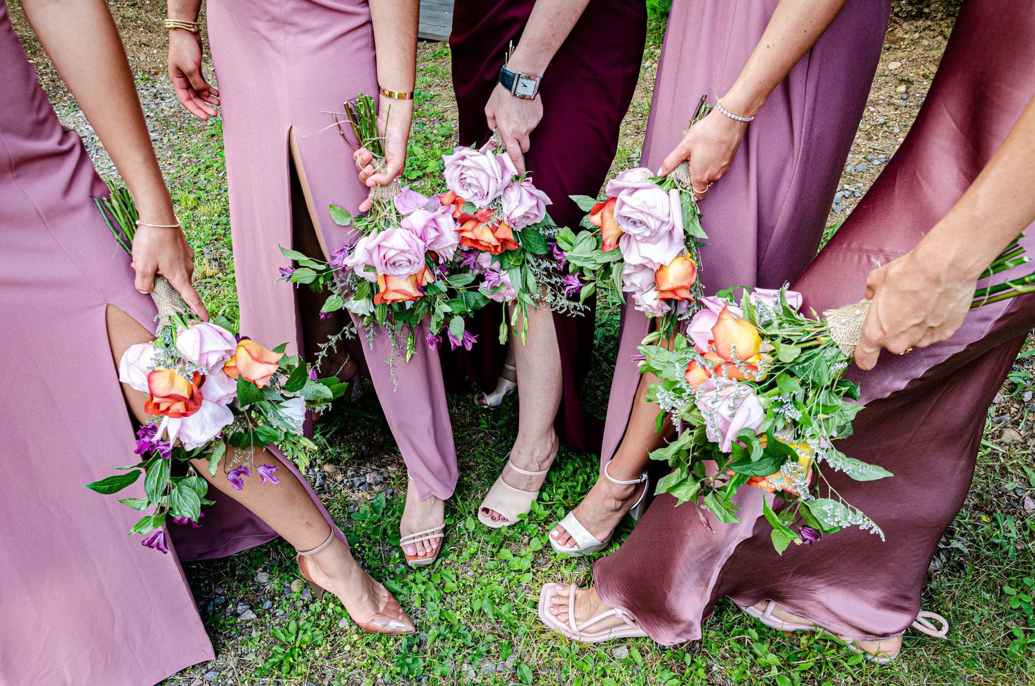 Detail shot of bridesmaids holding colorful bouquets while wearing mauve and burgundy dresses.