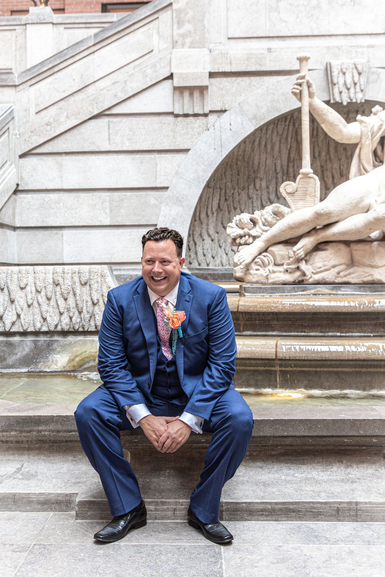 A series of photos showing someone in a navy blue suit posing casually near an ornate stone fountain.
