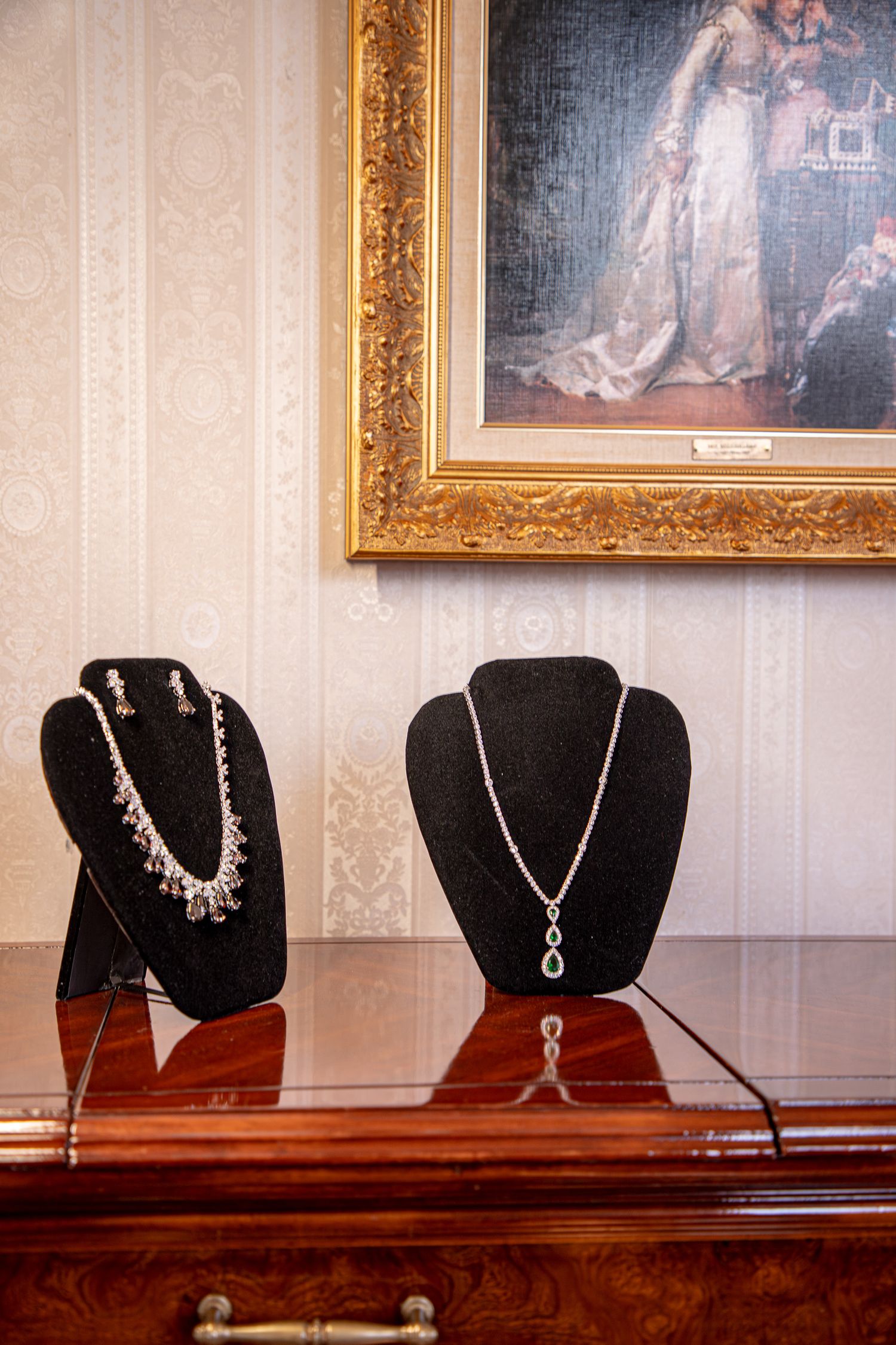 Elegant necklaces and pendants displayed on black velvet stands against a white wall with framed artwork.