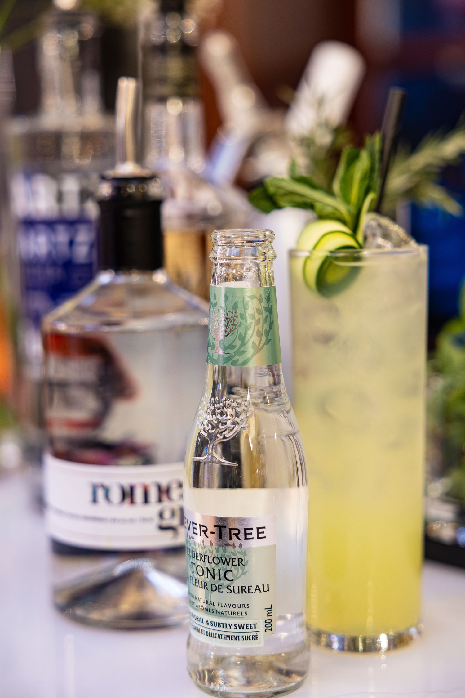 Close-up shots of Fever-Tree tonic water bottles and refreshing citrus cocktails on a bar counter with blurred background.