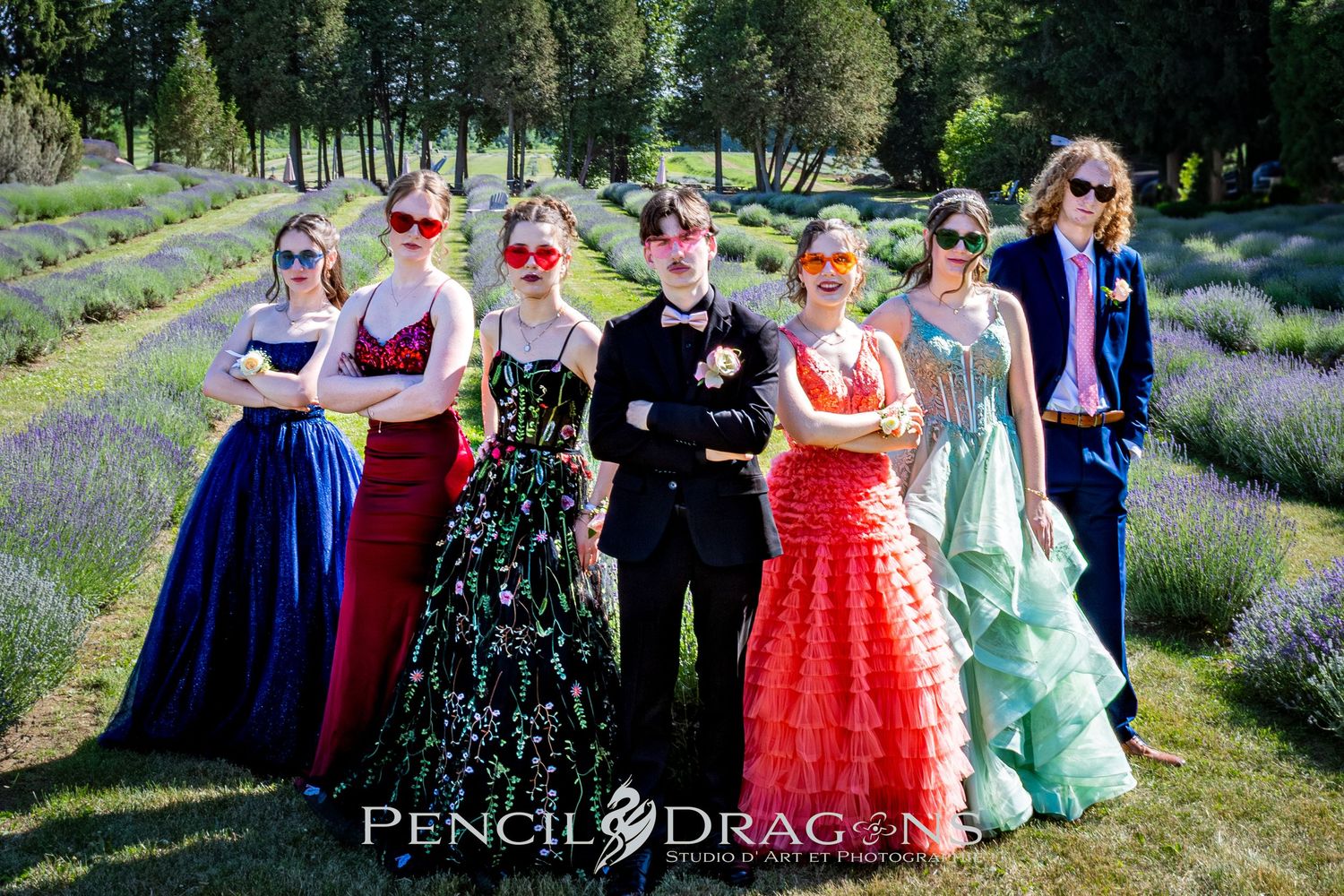 Large group photo of formal event attendees in colorful dresses and suits posing in a lavender field.