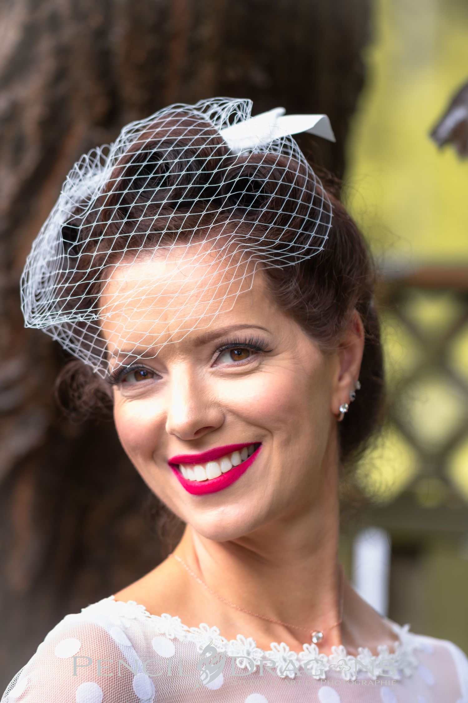 A classic bridal portrait showcasing a vintage-style birdcage veil and bright red lipstick.