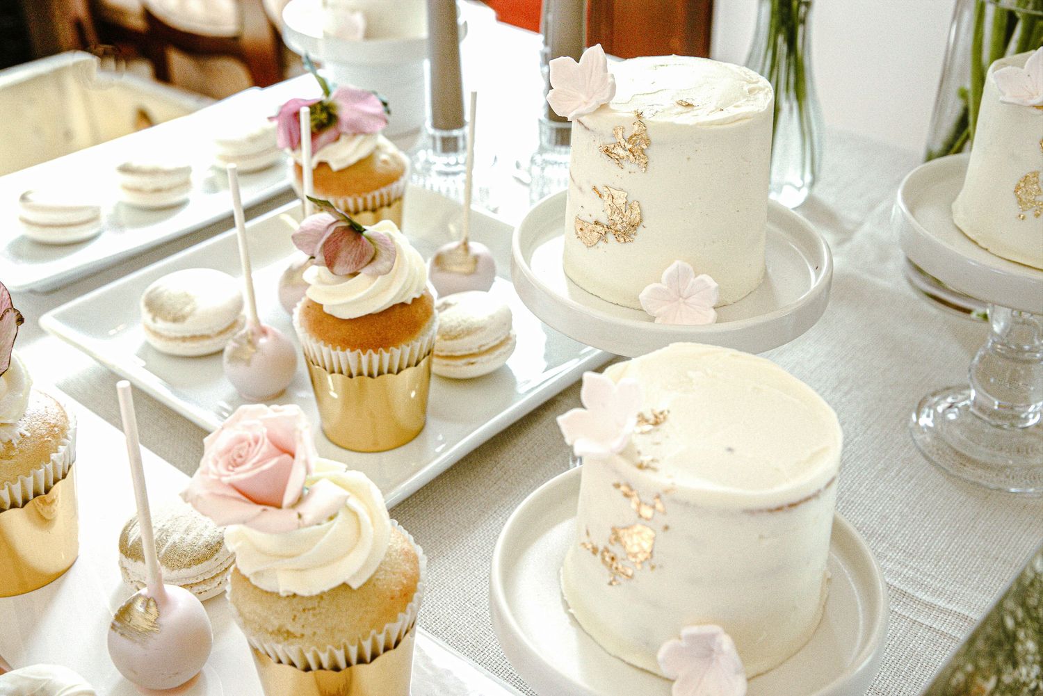 Elegant table setting with white cupcakes, delicate teacups, and floral arrangements for an afternoon tea party.