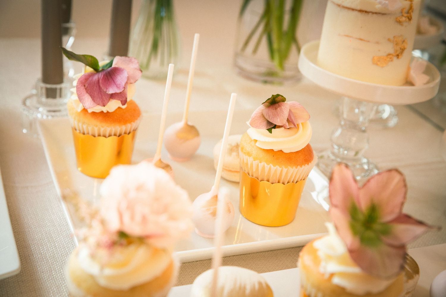 Elegant pink and peach cupcakes with floral decorations displayed on a white table with glowing candlelight.