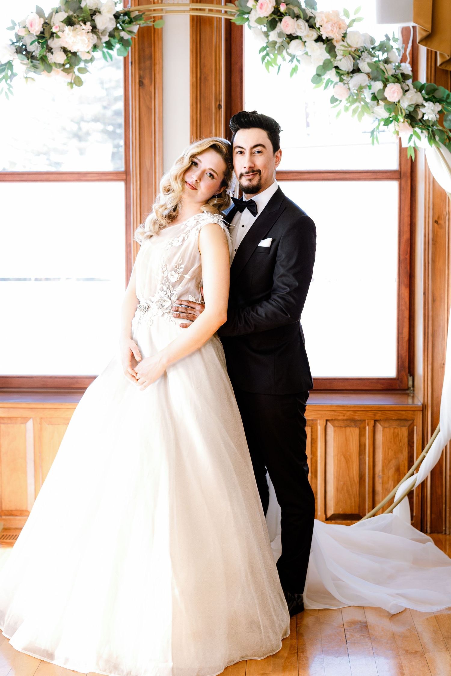 A romantic wedding couple shares intimate dance poses in an elegant wood-paneled room with floral decorations.