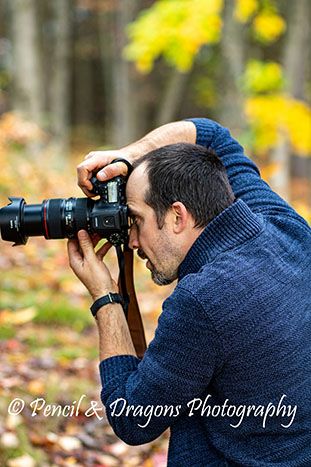 Photographer in blue sweater taking photos with telephoto lens in autumn forest setting.