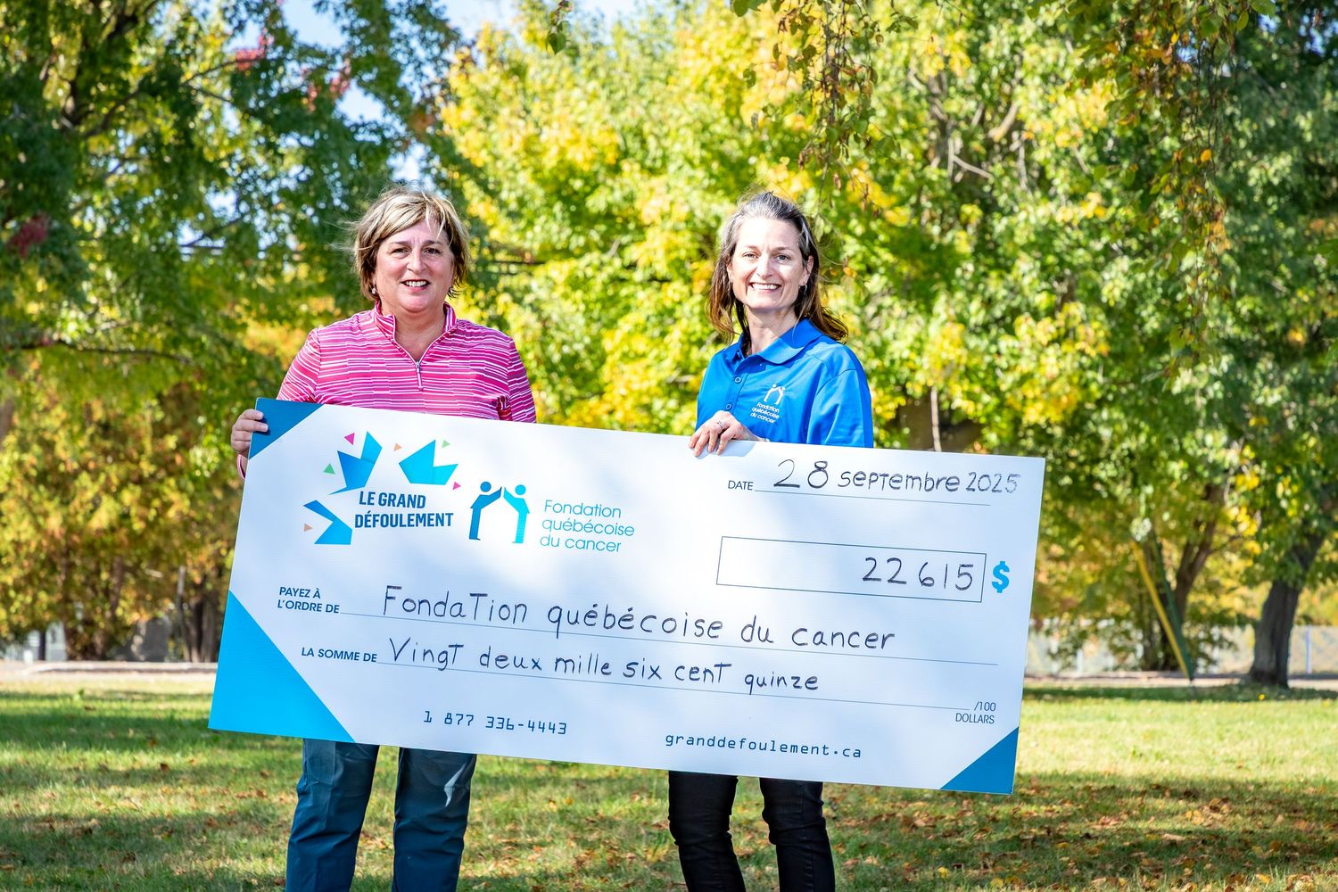 Two women proudly hold a large donation check for 22,615$ to Fondation québécoise du cancer outdoors.