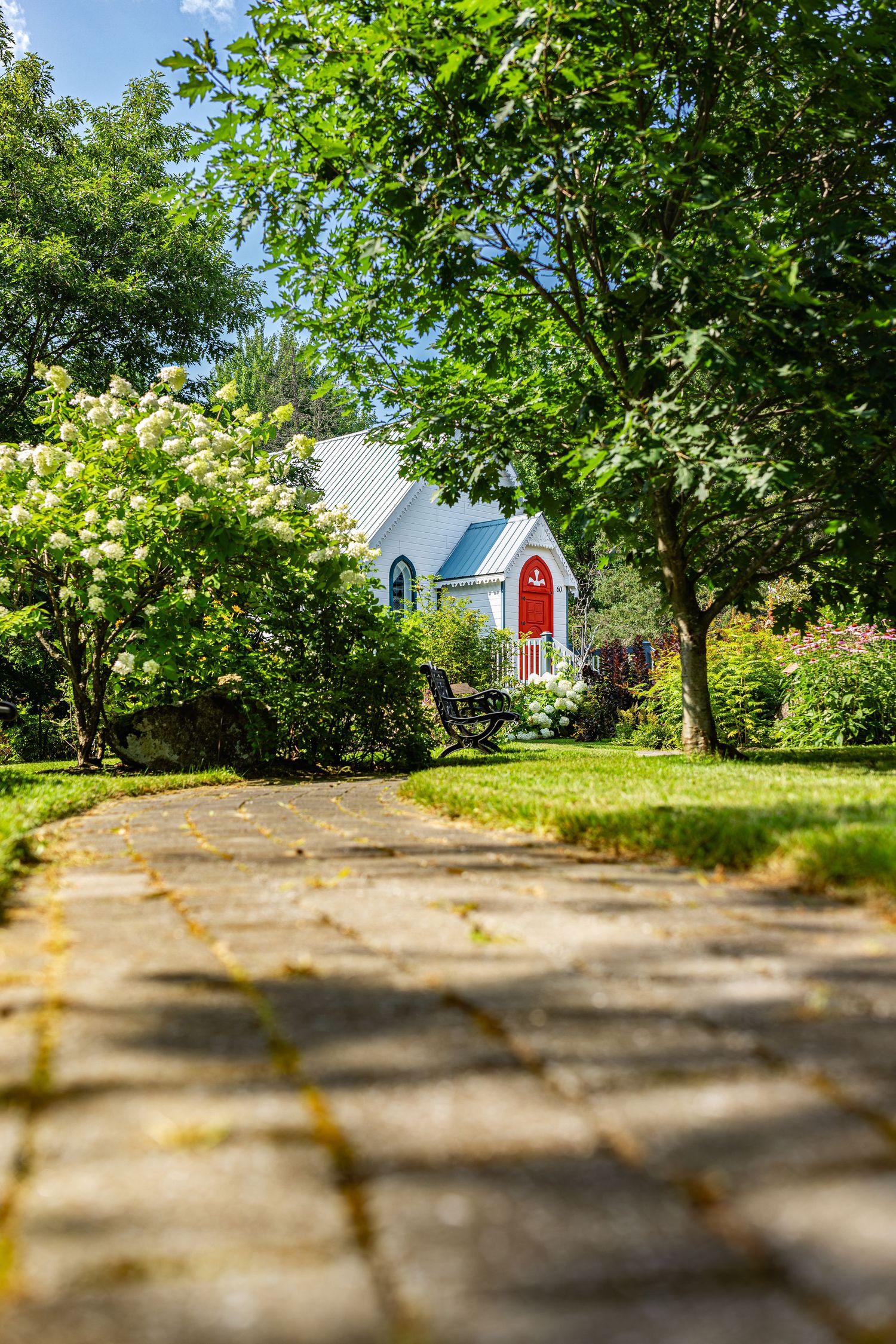 A panoramic view of a winding concrete pathway through a lush green garden with trees and a white house in the distance.
