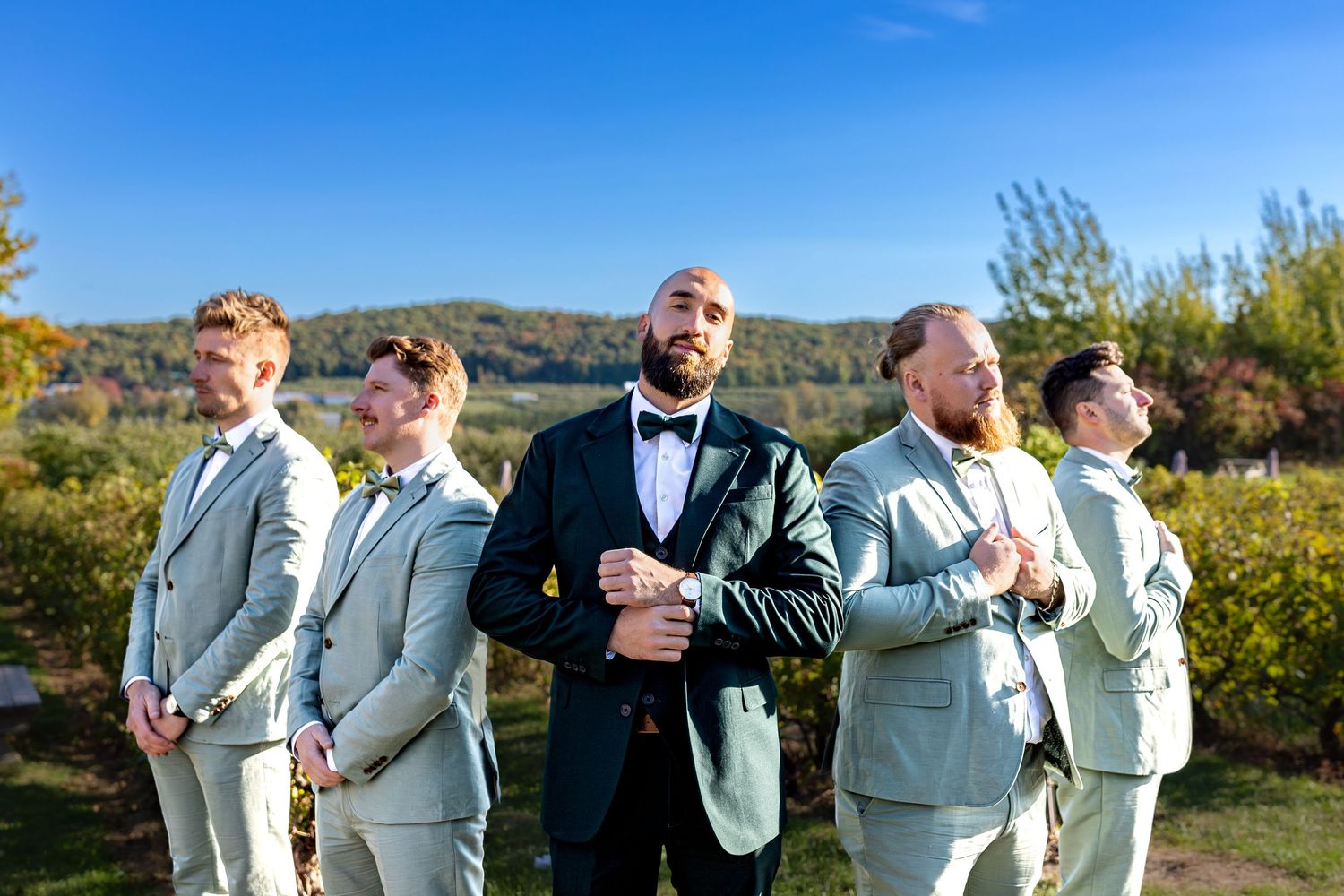 Groomsmen in light gray suits striking fun poses against autumn backdrop.