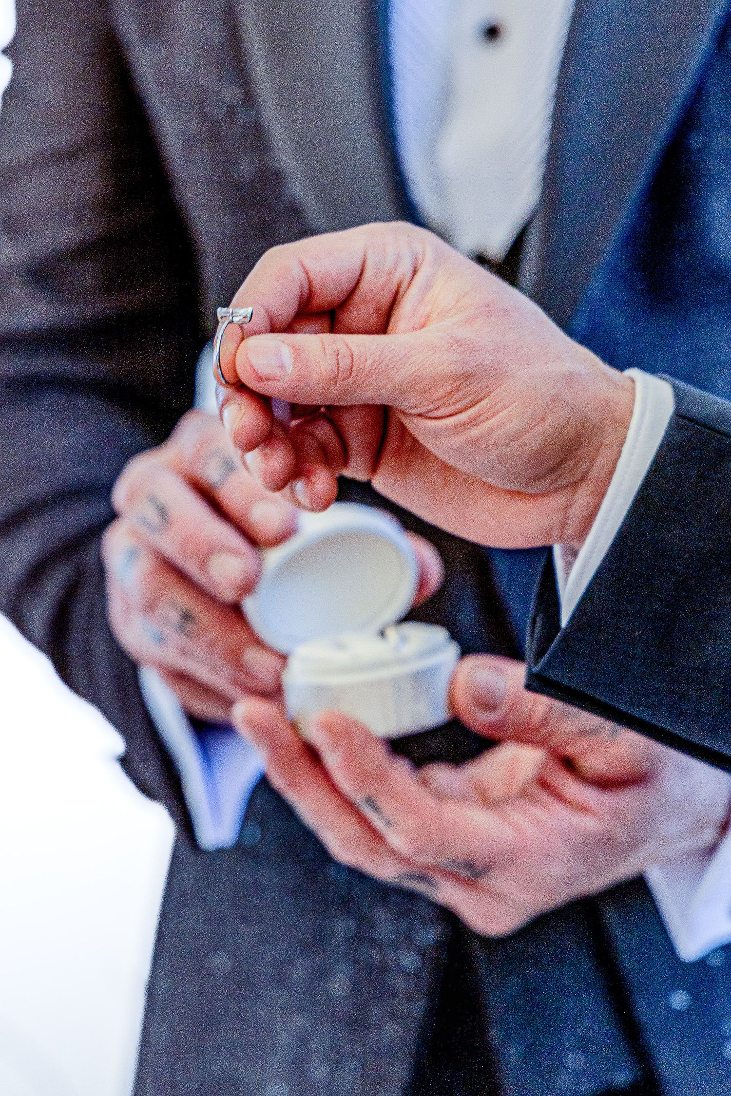 Hands in formal attire opening a small white container in a sequence of four close-up shots.