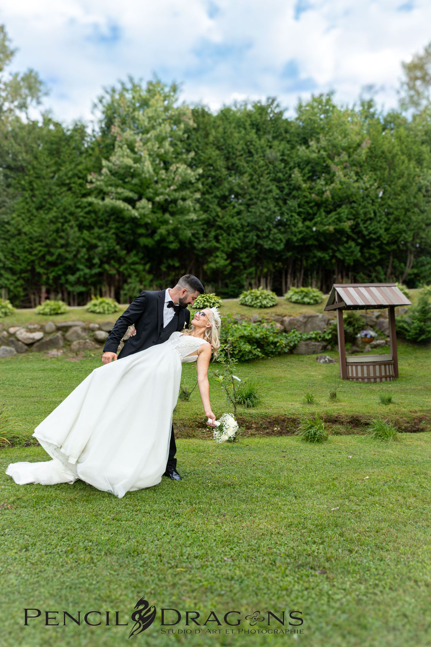 Wedding couple performs romantic dips on green lawn with garden scenery.
