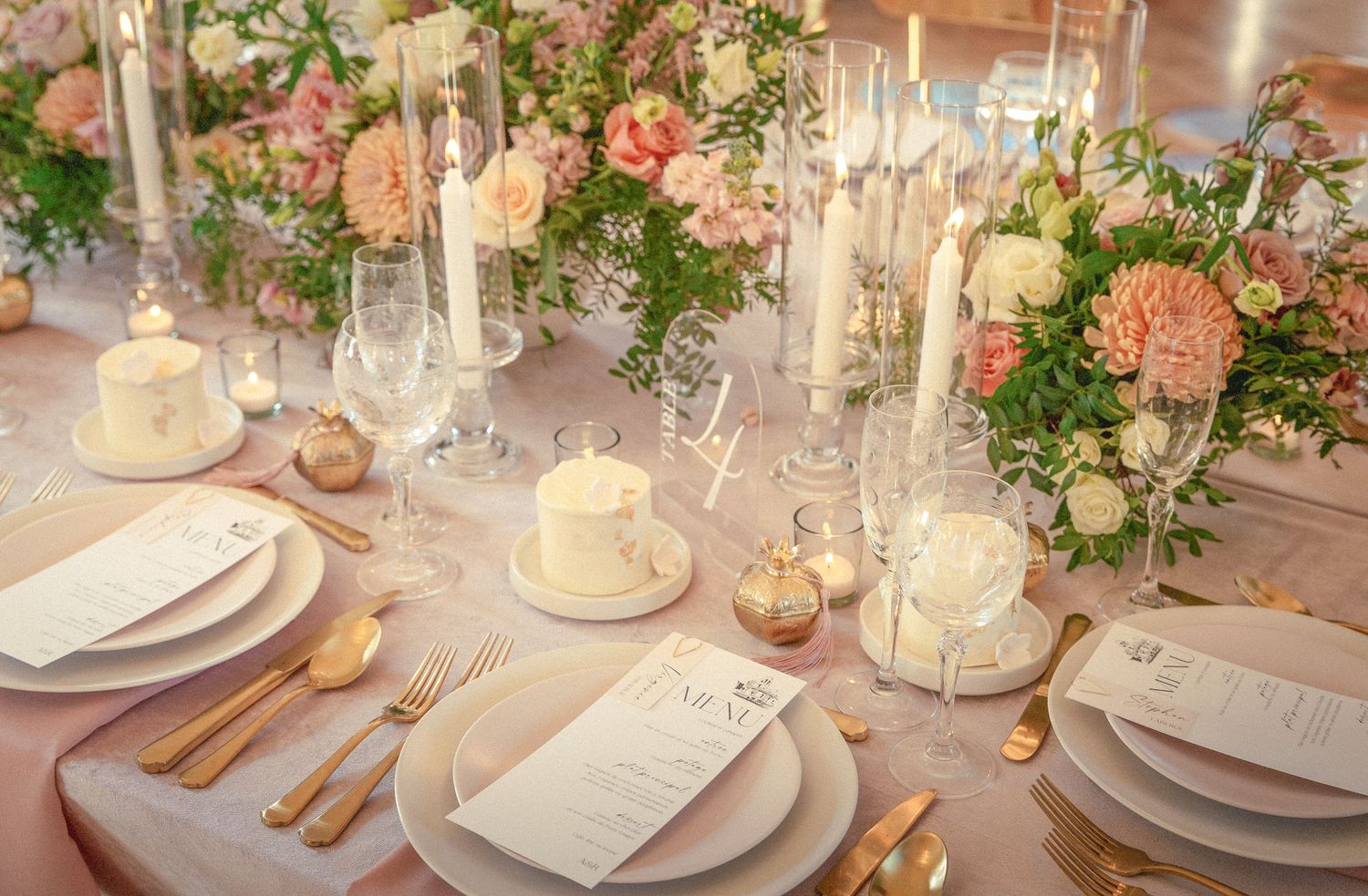 Elegant wedding reception table setting with white candles, blush flowers, and crystal glassware in warm lighting.