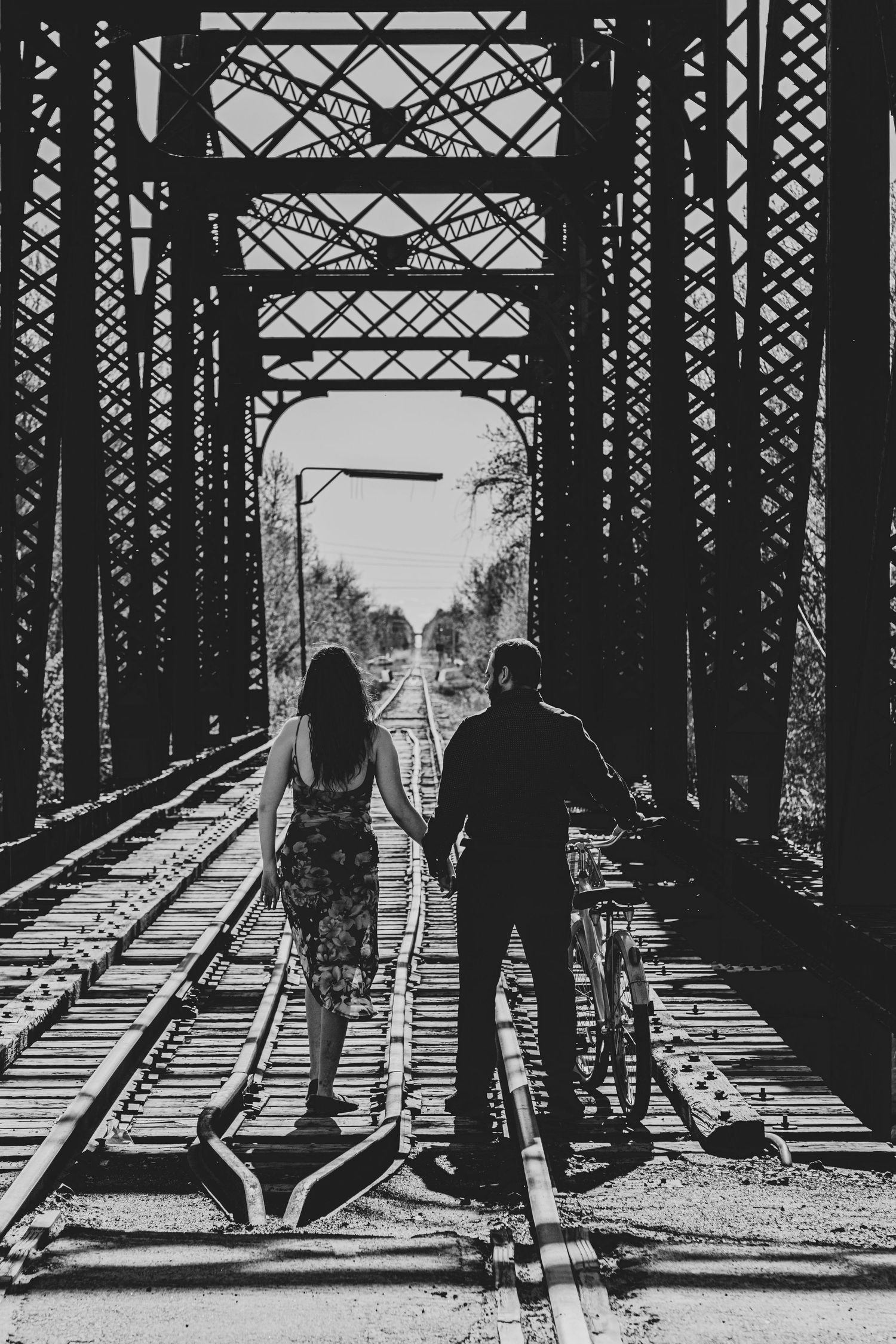 Black and white silhouettes of people standing on railroad bridge with dramatic industrial framing.