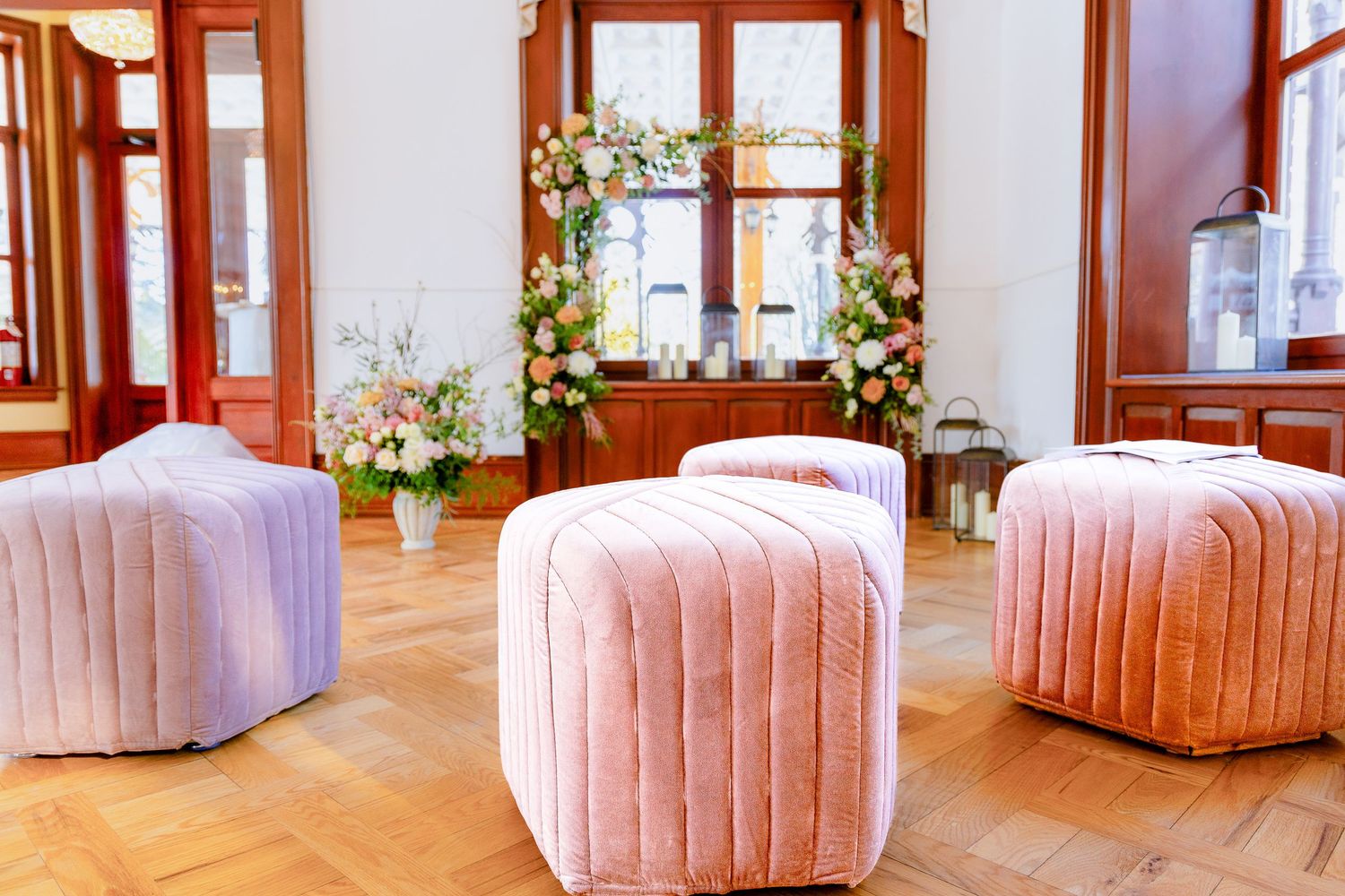 Pink velvet channel tufted ottoman bench with curved back in a bright sunlit room with wooden floors.