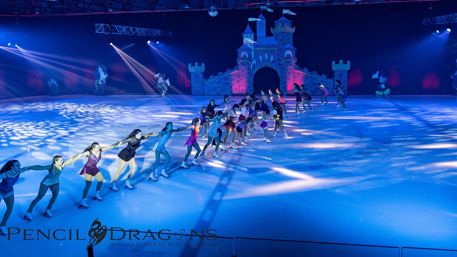 Ice skaters perform in a spectacular Disney-themed ice show with colorful blue lighting and a castle backdrop.