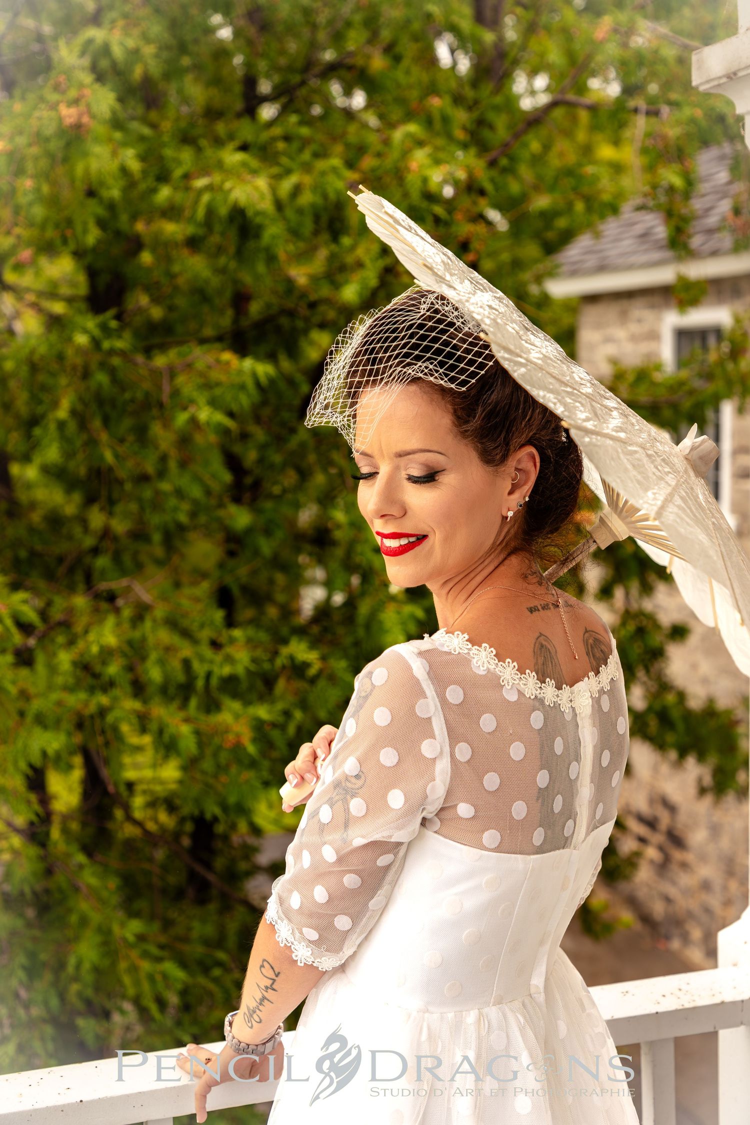 A vintage-style bridal portrait featuring a white polka dot dress and parasol in a garden setting.