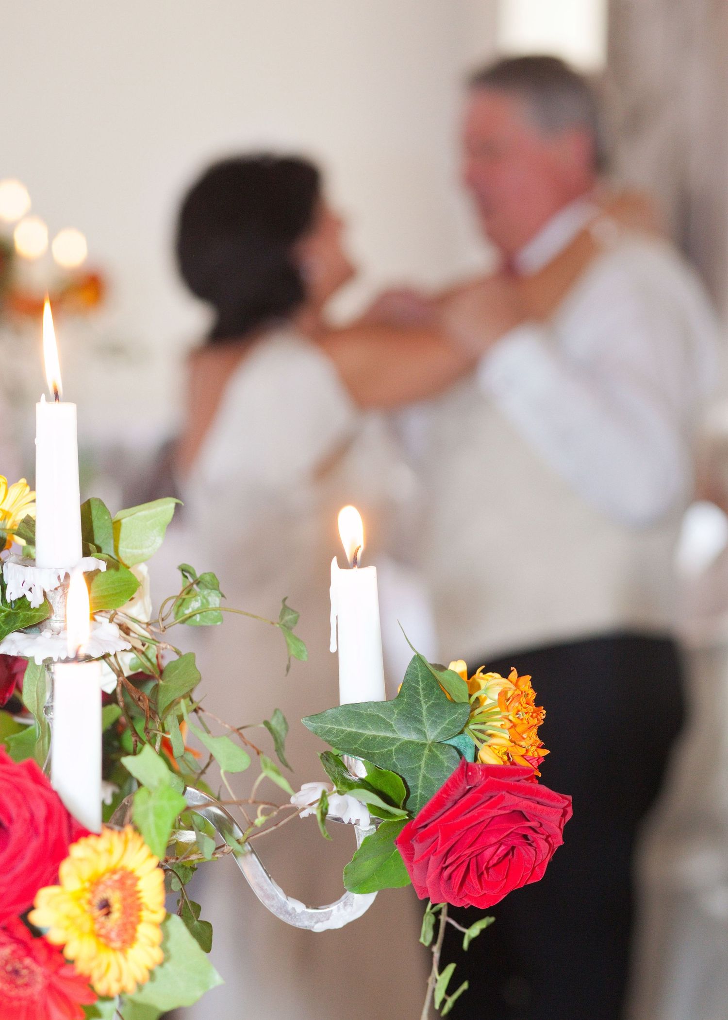 Elegant table centerpiece with white candles, red roses and yellow flowers.