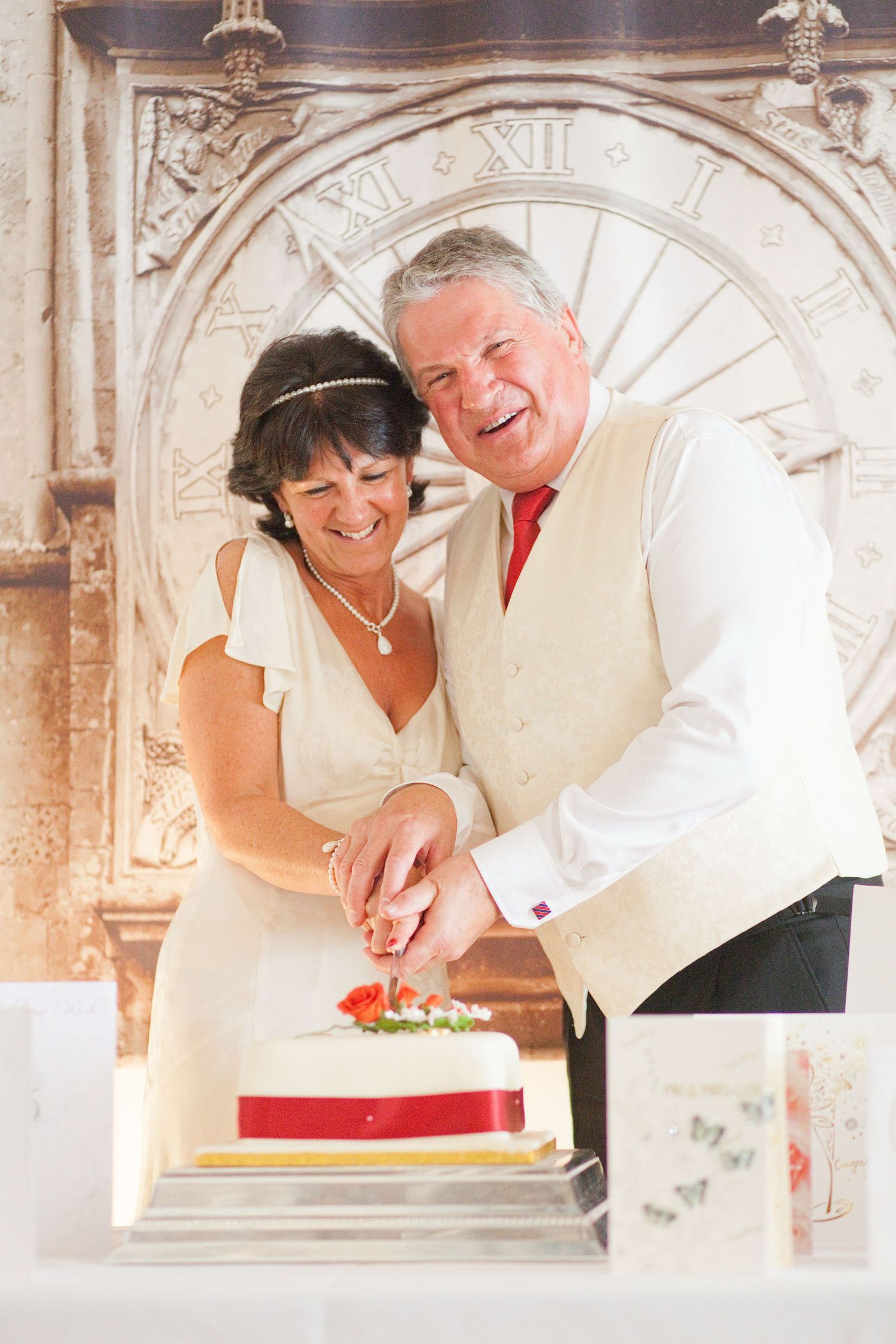 A couple cuts into their wedding cake together in an ornate venue with decorative architecture.