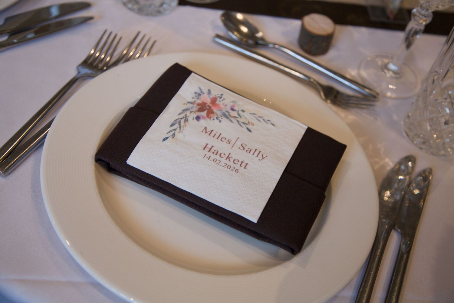 Elegant place settings with name cards and silverware on white tablecloths at wedding reception.