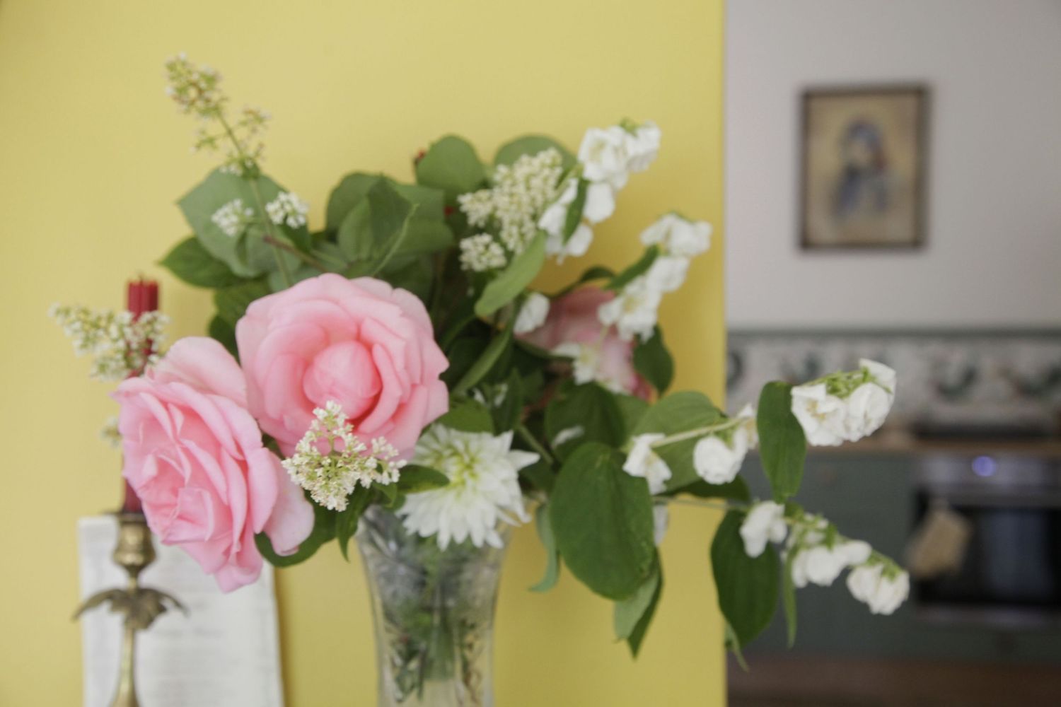 Pink and white floral arrangements in glass vases displayed on a table against a yellow wall.