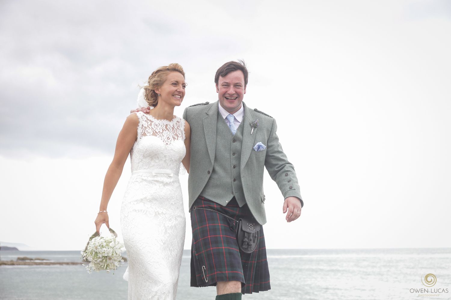 Joyful wedding portraits taken along a scenic seaside with dramatic coastal views.