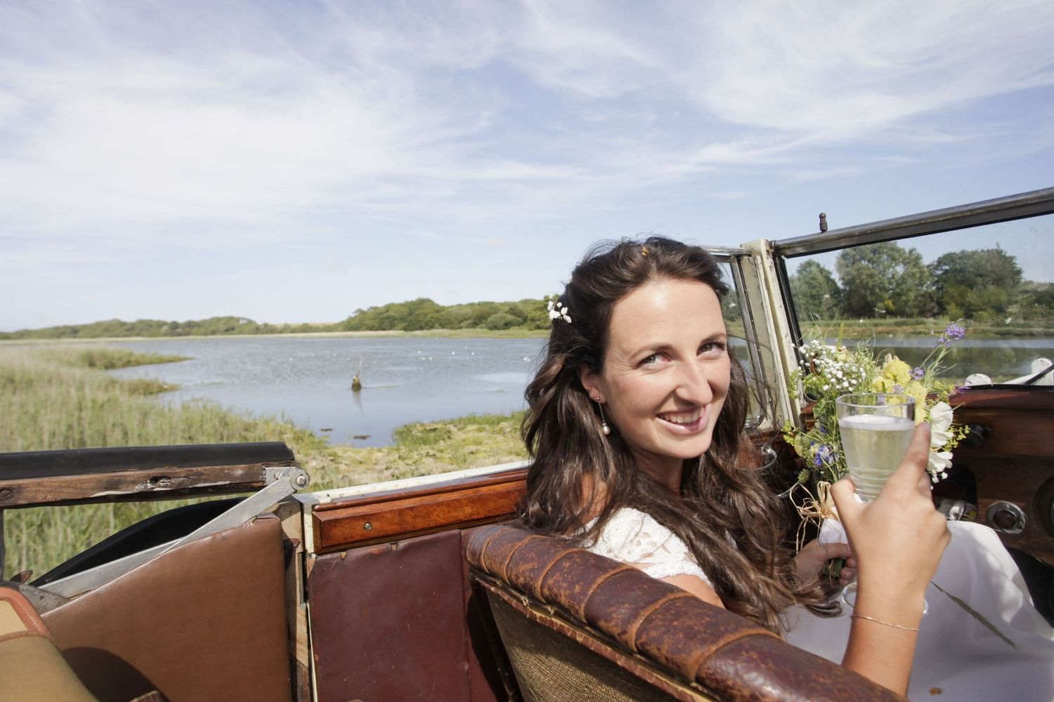Bride by the sea in a convertible open top vintage wedding car during their beach wedding bridal photo shoot.