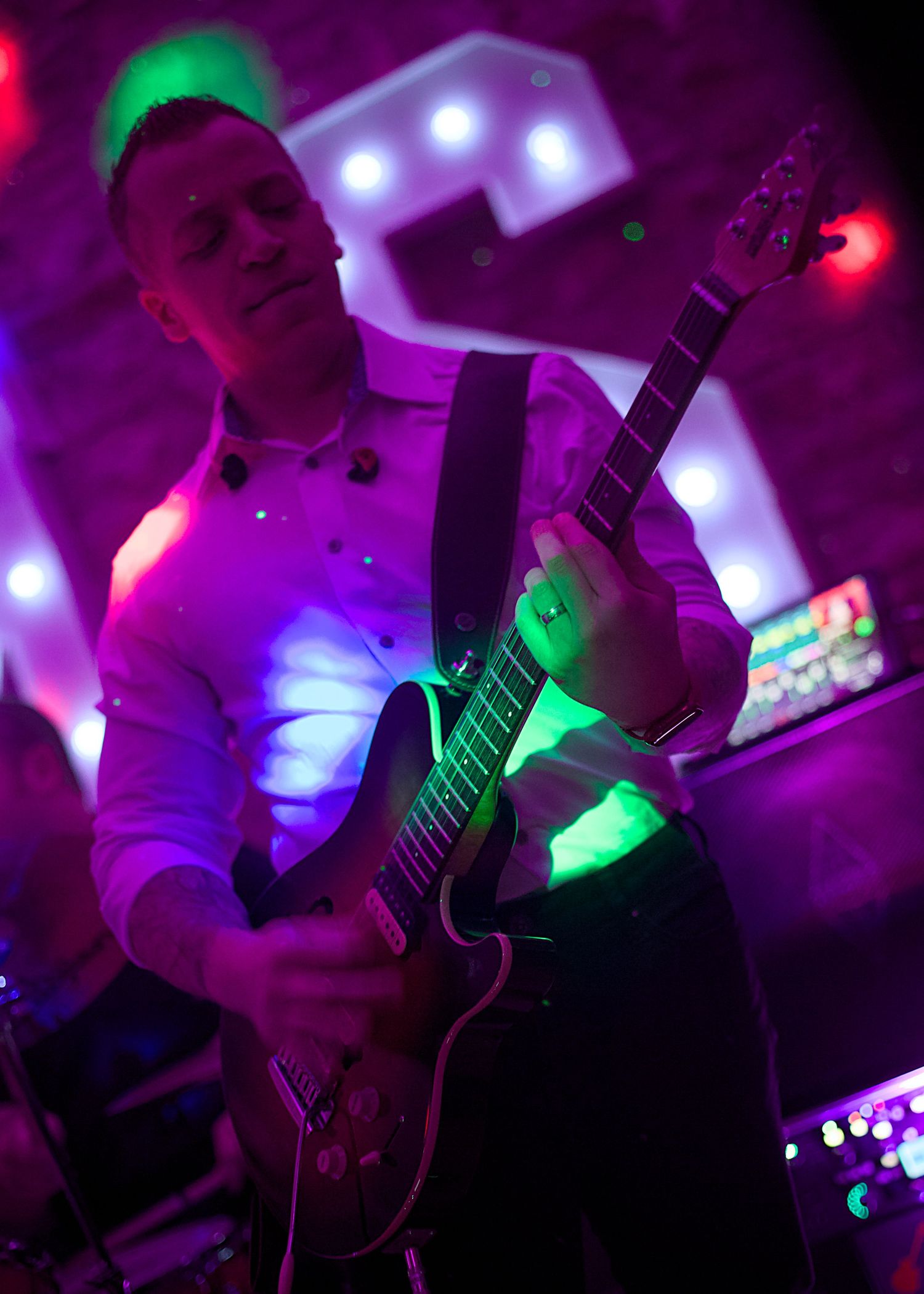 Musicians of Freeze at Folly Farm Somerset wedding perform on stage under vibrant purple and green lighting at a live event.