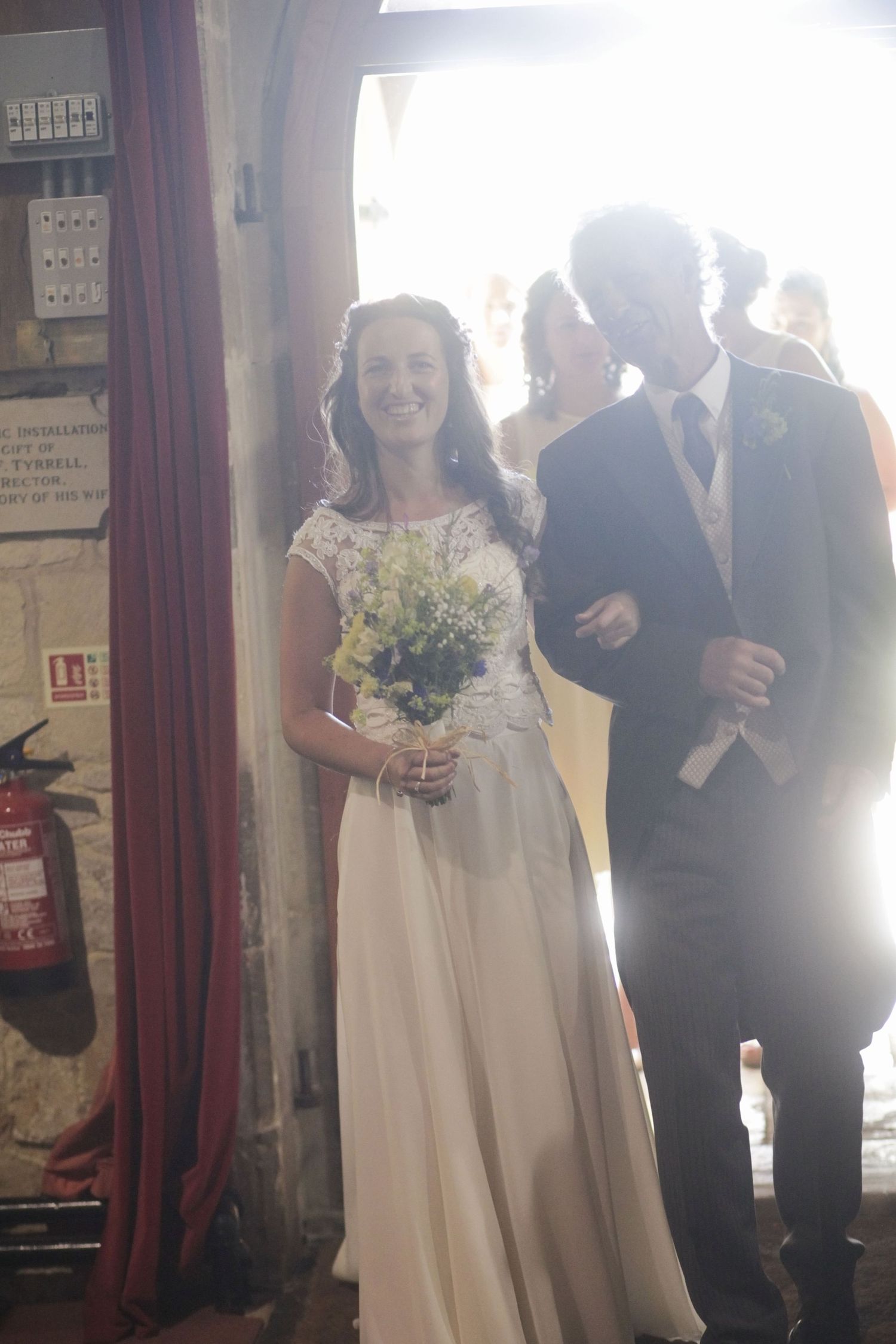 Wedding party members walking down the aisle in a sunlit church interior.