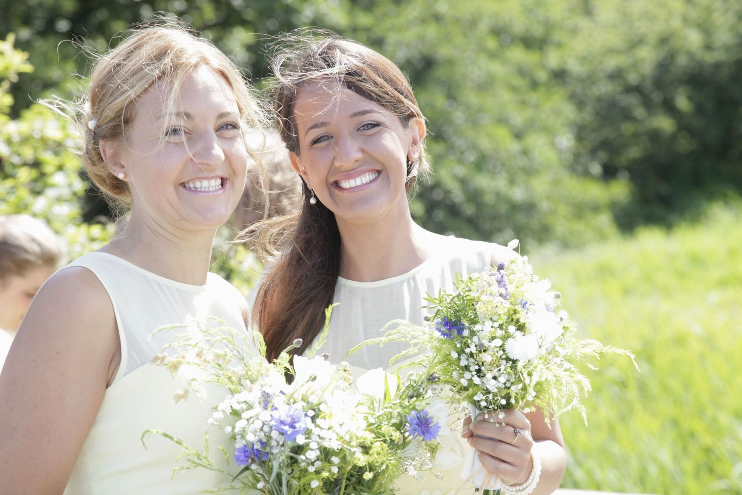 Wedding attendants share candid moments of laughter in a sunny outdoor setting.