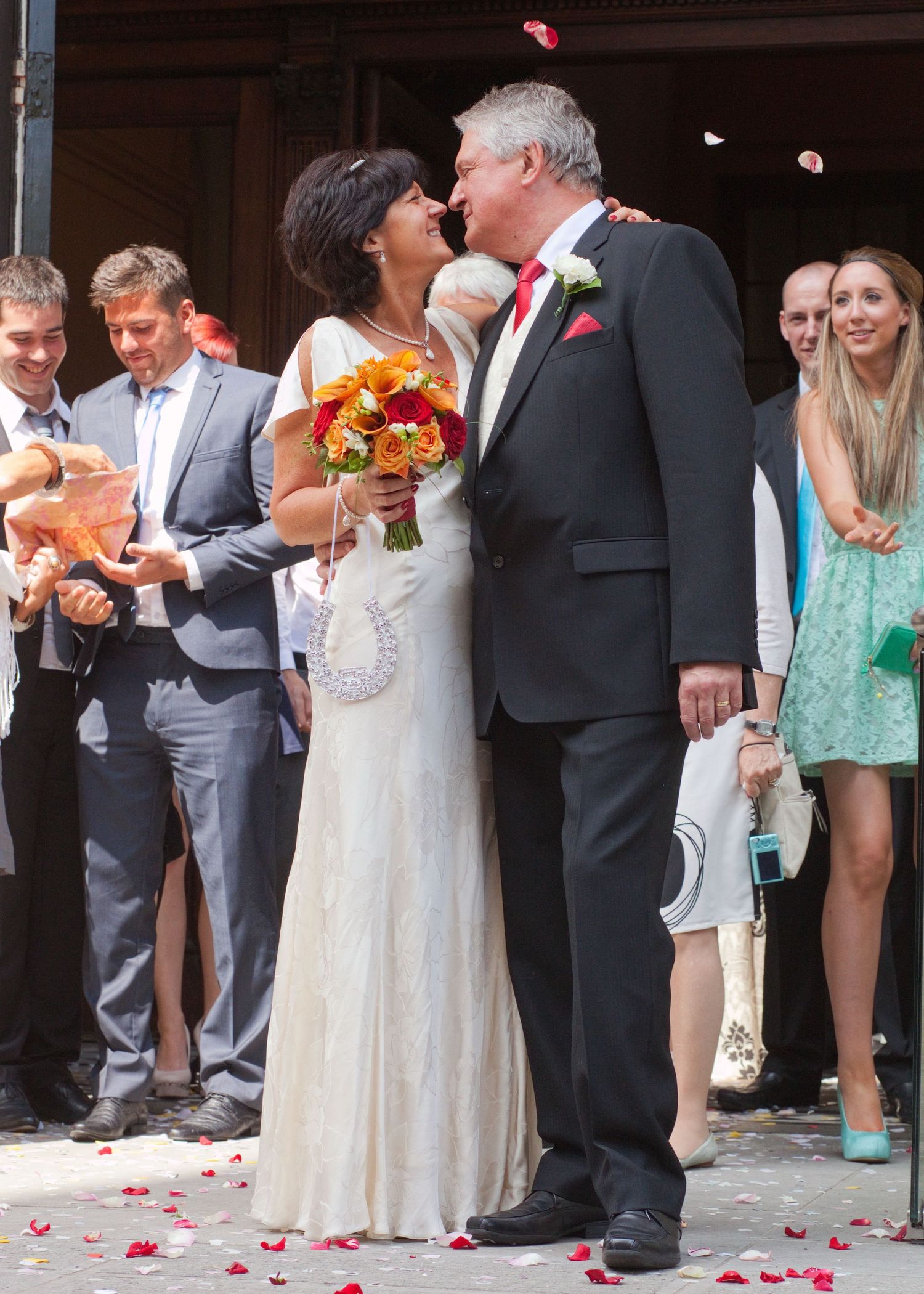 A wedding couple sharing a romantic moment as guests watch and rose petals fall.