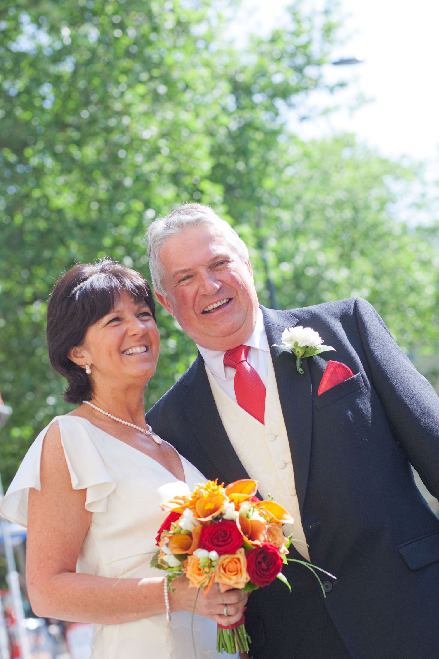 Candid wedding photos showing joyful laughter between couple with bright floral bouquet outdoors.